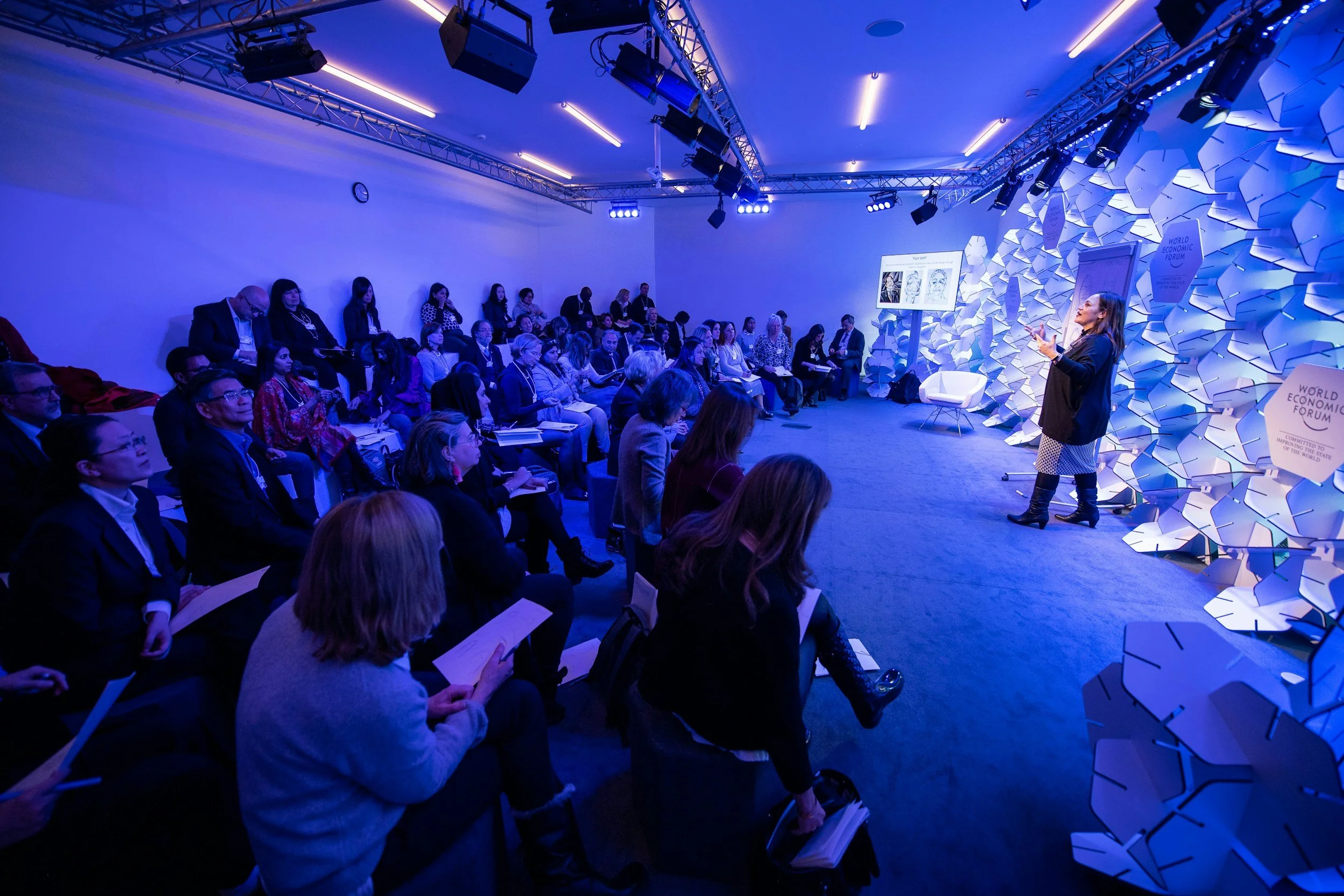 A speaker giving a presentation in a dim lit conference room