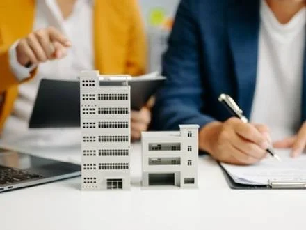 Model of a city with tall buildings on a table, with people in business attire working in the background.