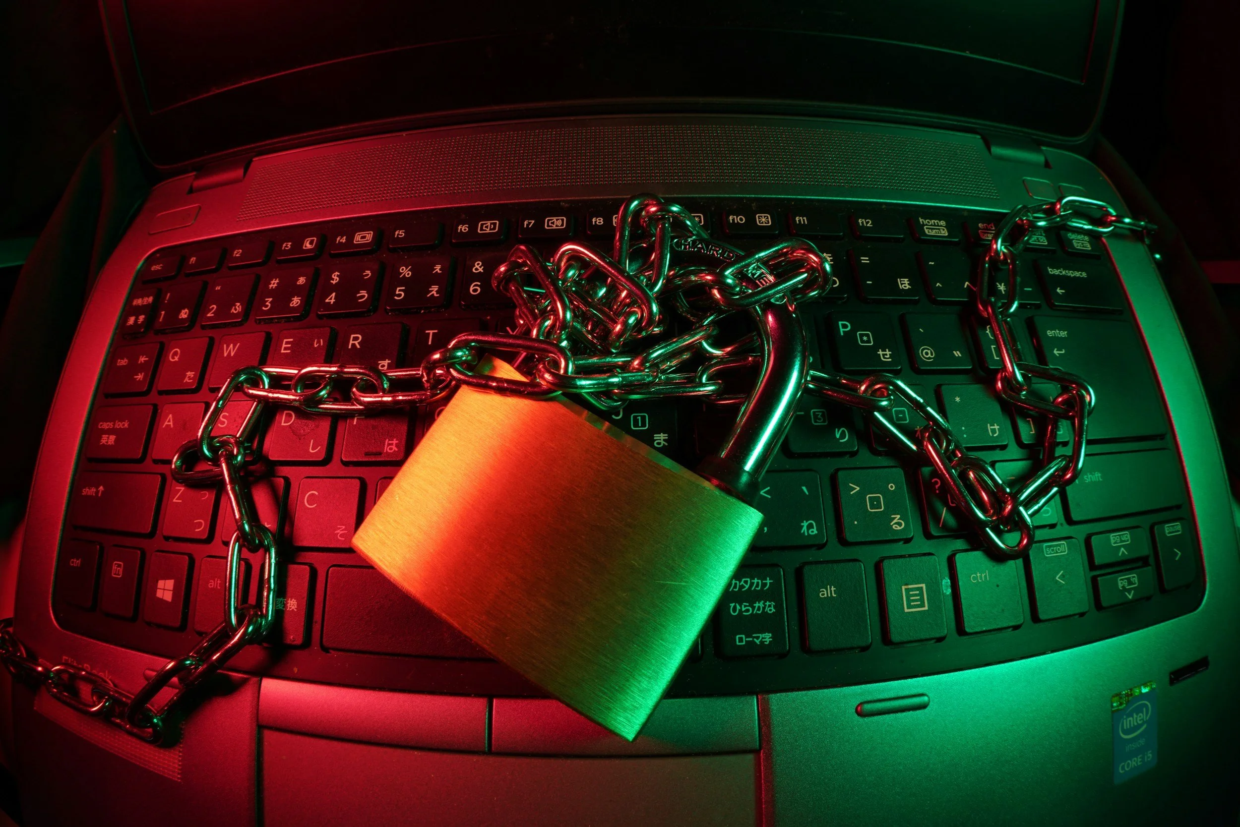 A laptop keyboard with a thick chains and a padlock placed on top, under green and red lighting.