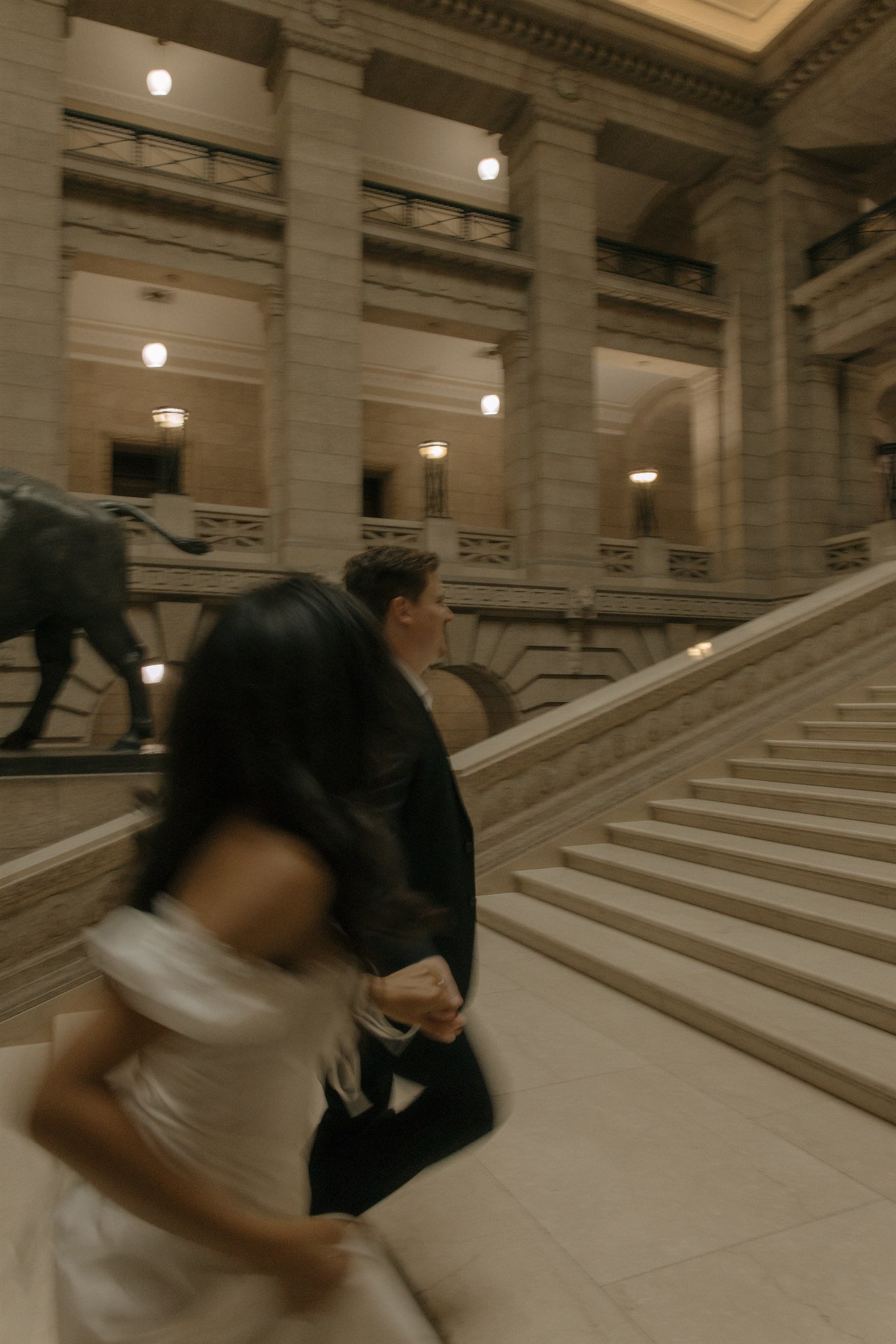 People walking up the staircase inside a grand, historic building with large columns and ornate architecture.