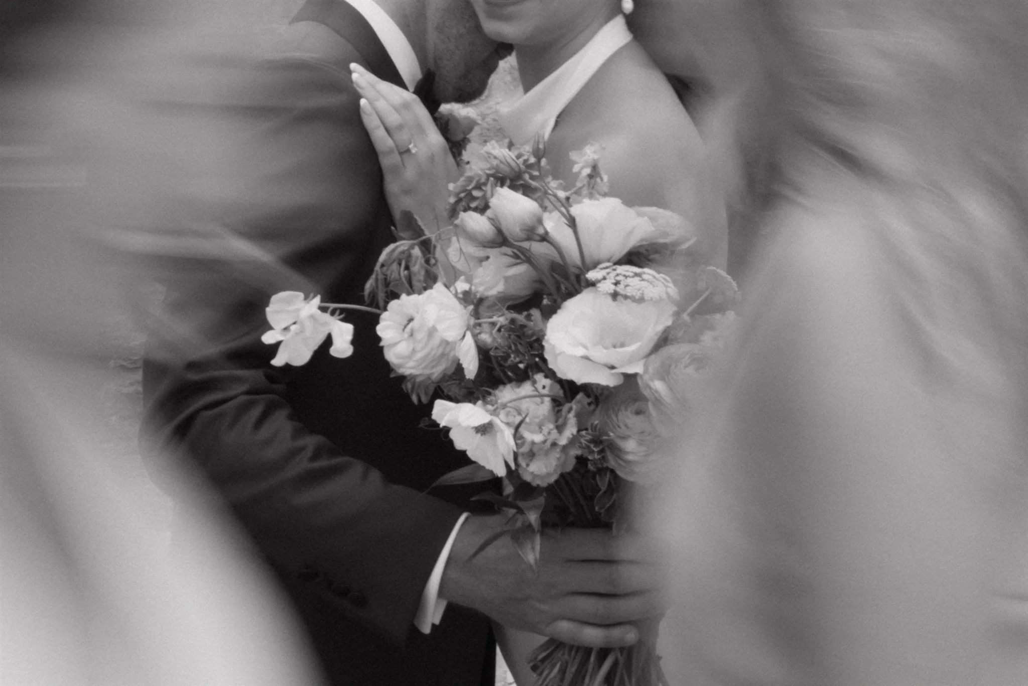 A black and white photo of a bride and groom hugging, with the bride holding a bouquet of flowers.