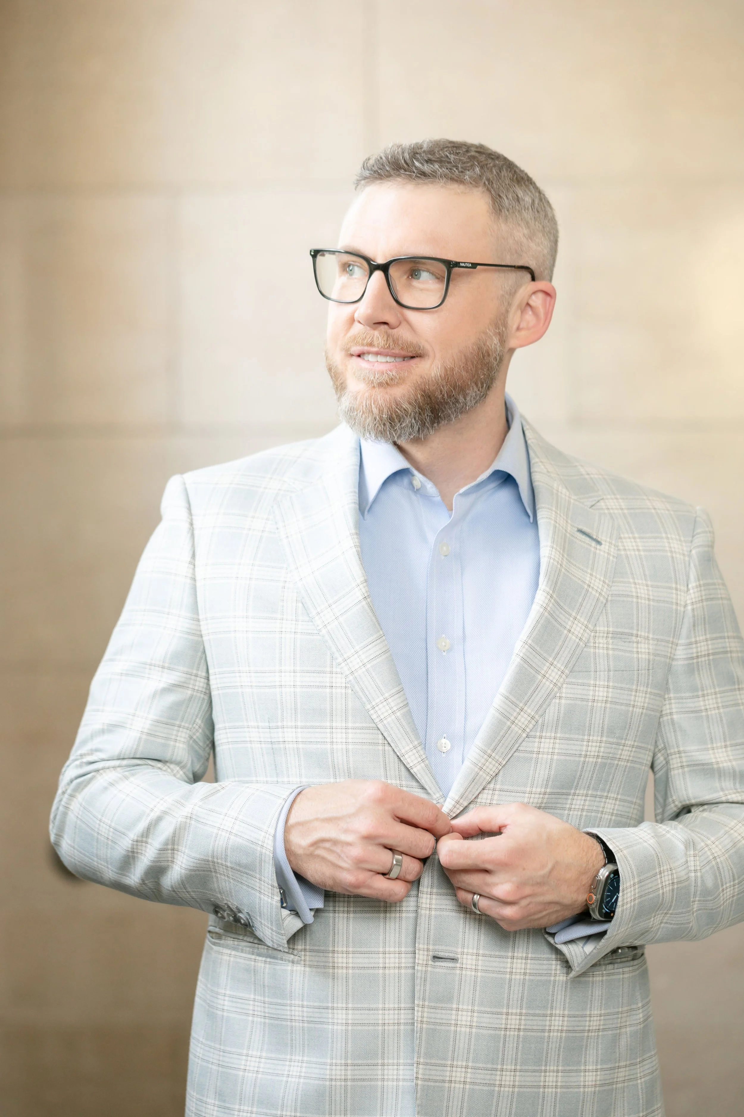 Attorney wearing a light colored suit and blue shirt poses for a headshot while adjusting his suit button