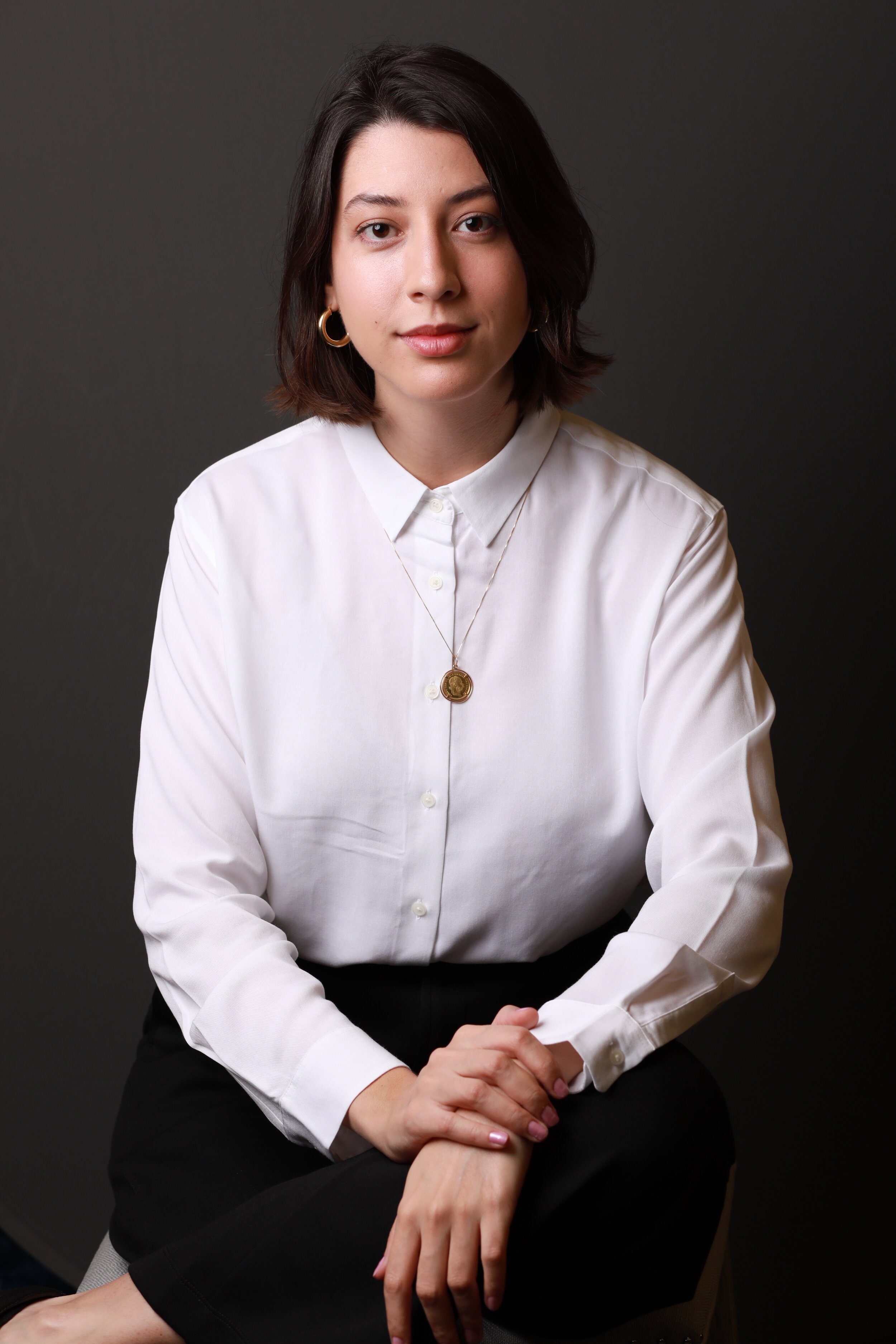 Portrait of a woman with dark, short hair wearing a white blouse and gold earrings
