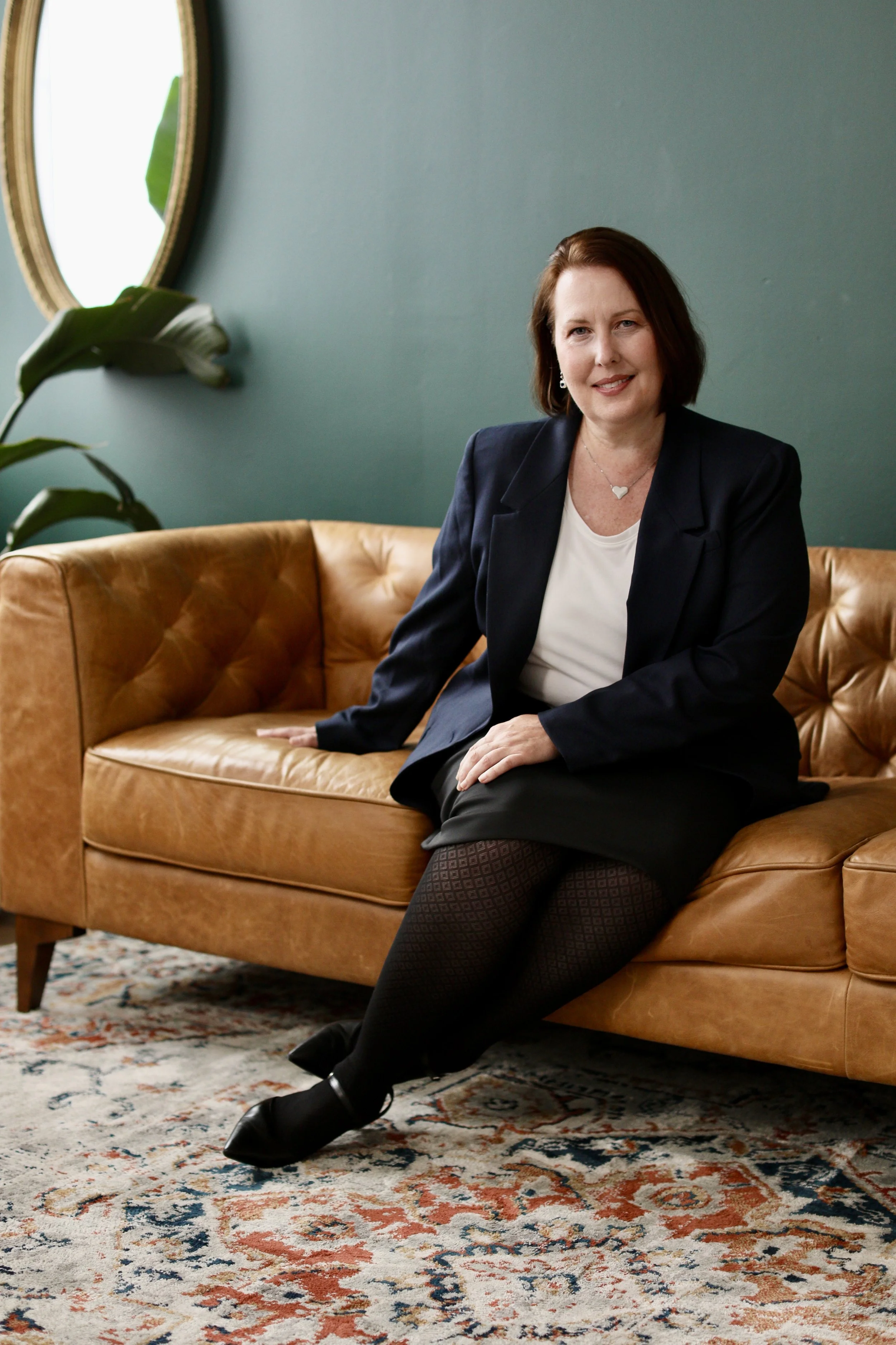 professional headshots for women elevate your personal brand. woman business owner sits on a camel-colored leather couch set in a boho style room