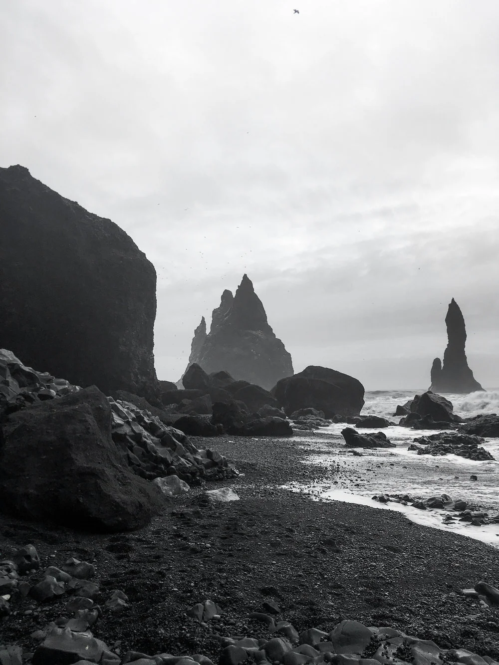 Black and white photo of a rocky coastal scene with large sea stacks and cliffs on an overcast day.