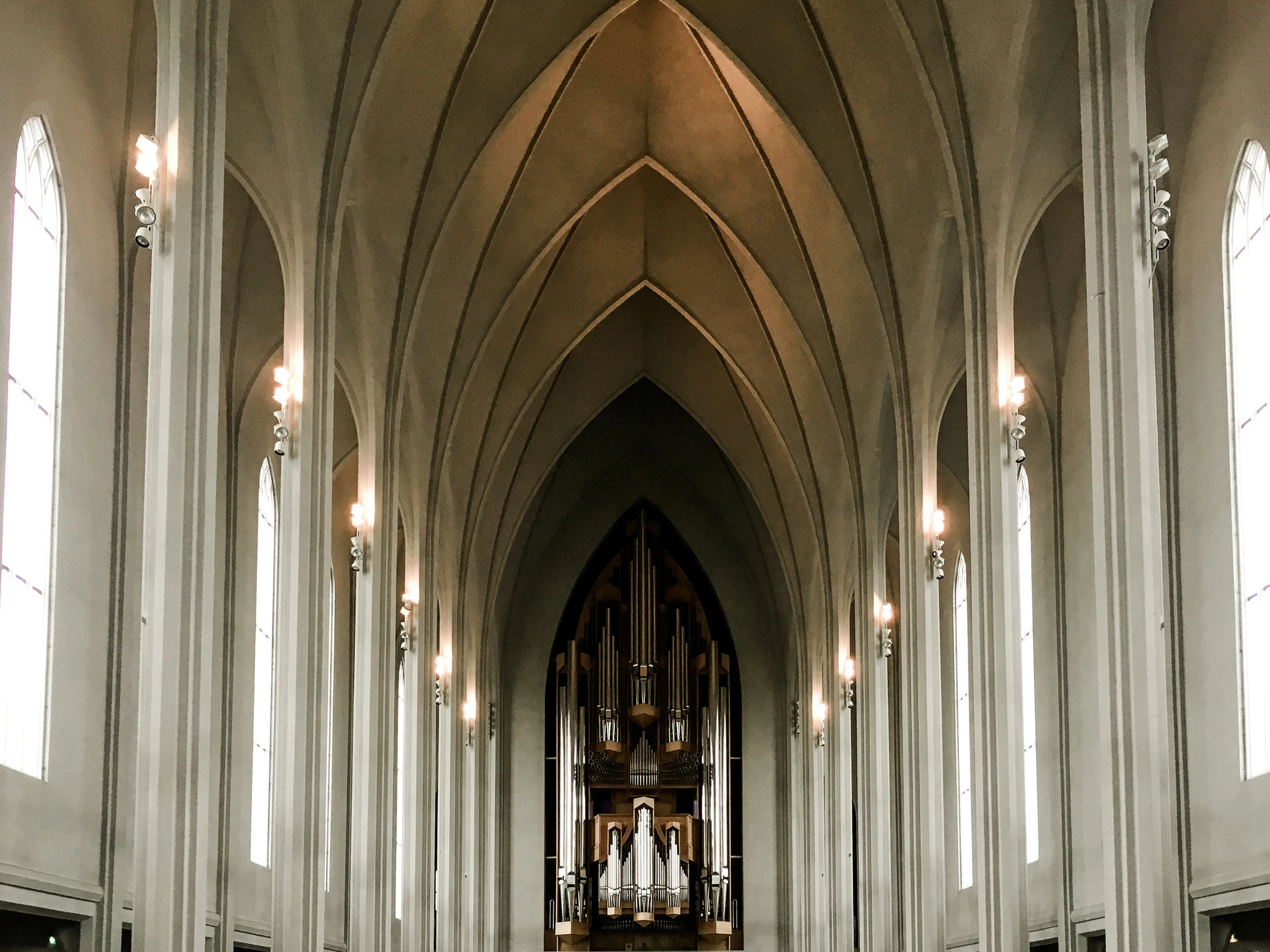 Interior of a church with tall pointed arches, large windows, and an organ at the front.