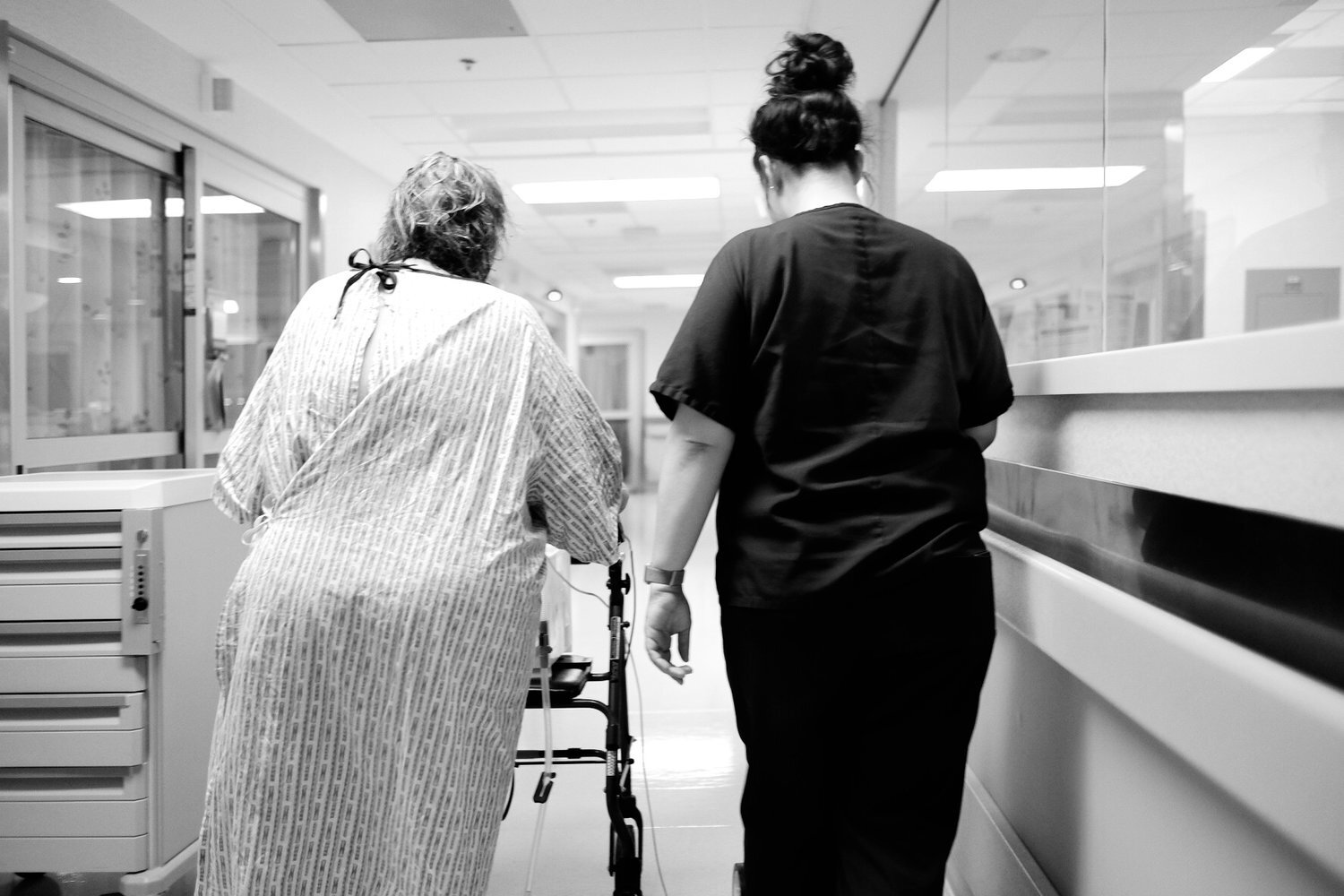 A nurse guides her patient down a hallway. Photojournalism photos document a patient's post-op recovery after heart surgery
