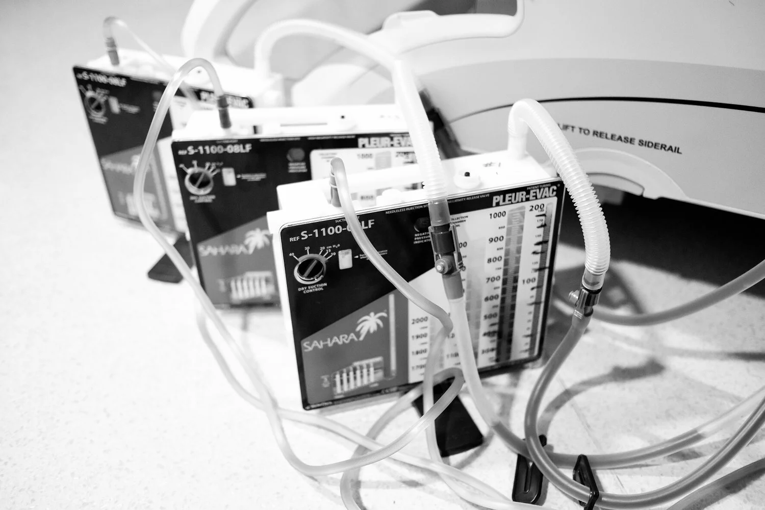 Three portable medical suction devices with tubes on a counter next to a white medical machine.