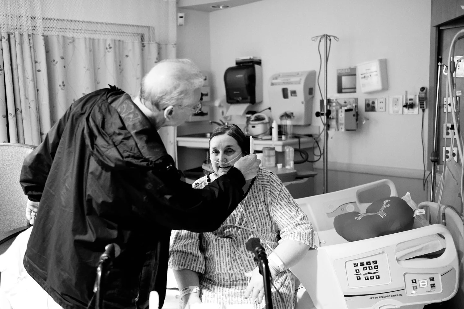 A person in a hospital bed with a nasal cannula, being cared for by an visitor or caregiver in a hospital room.
