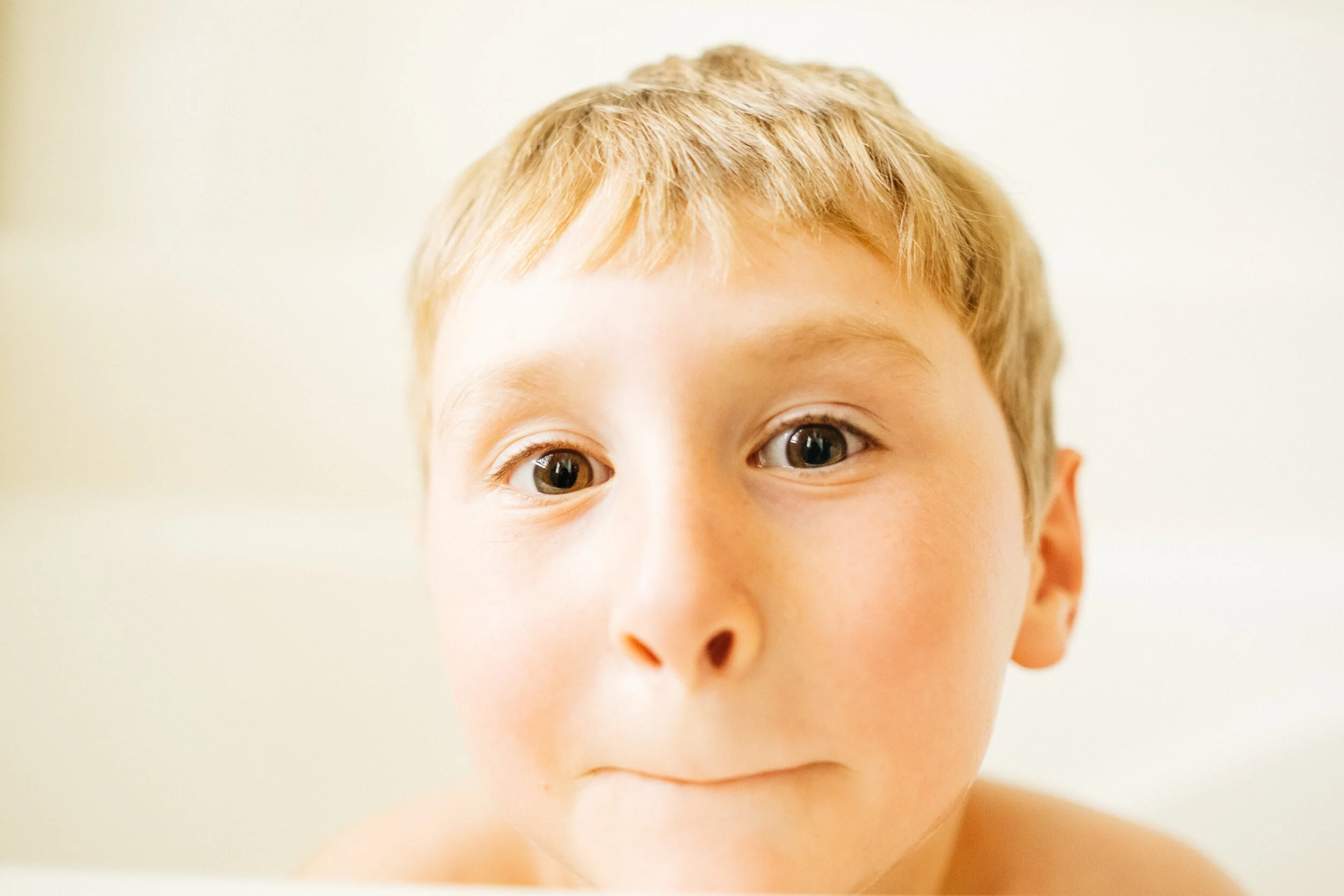 A close-up portrait of a young boy with light skin and blonde hair, looking directly at the camera with a neutral expression.