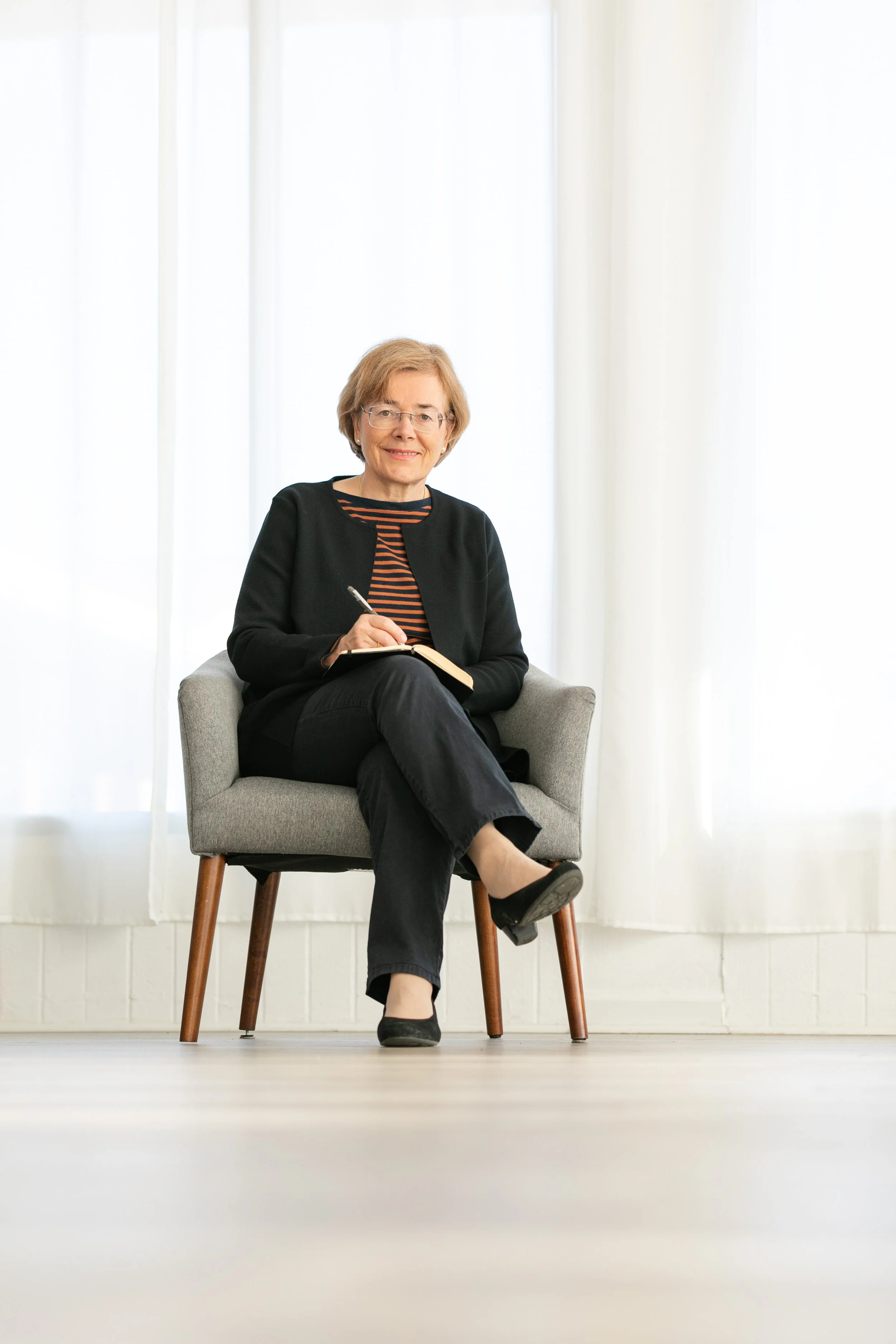 A middle-aged female psychiatrist with short, blonde hair takes notes on her notepad by hand to demonstrate how she interacts and listens to her mental health patients
