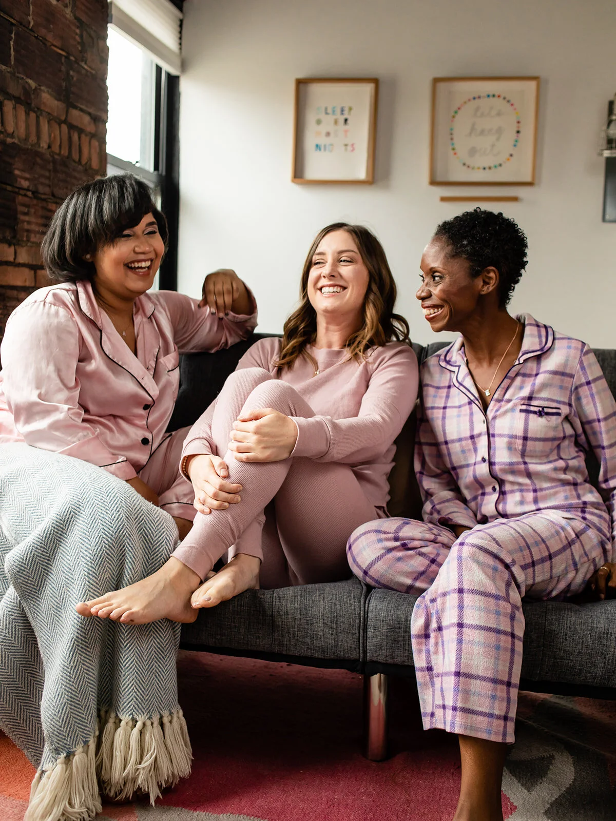 Three women wearing pink pajamas are sitting on a couch and laughing 