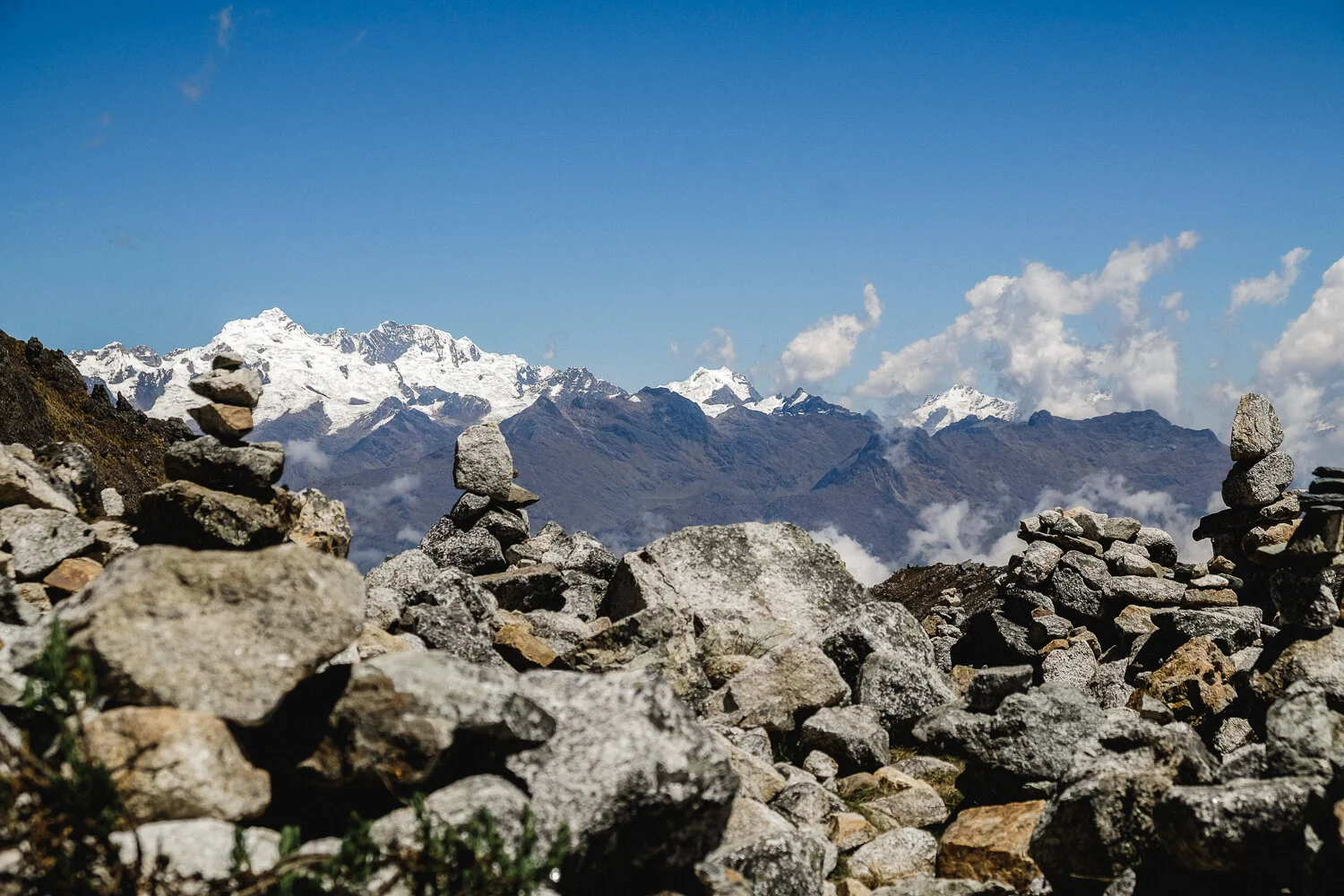 Stacked rocks in the foreground with snow-capped mountains and a blue sky in the background.