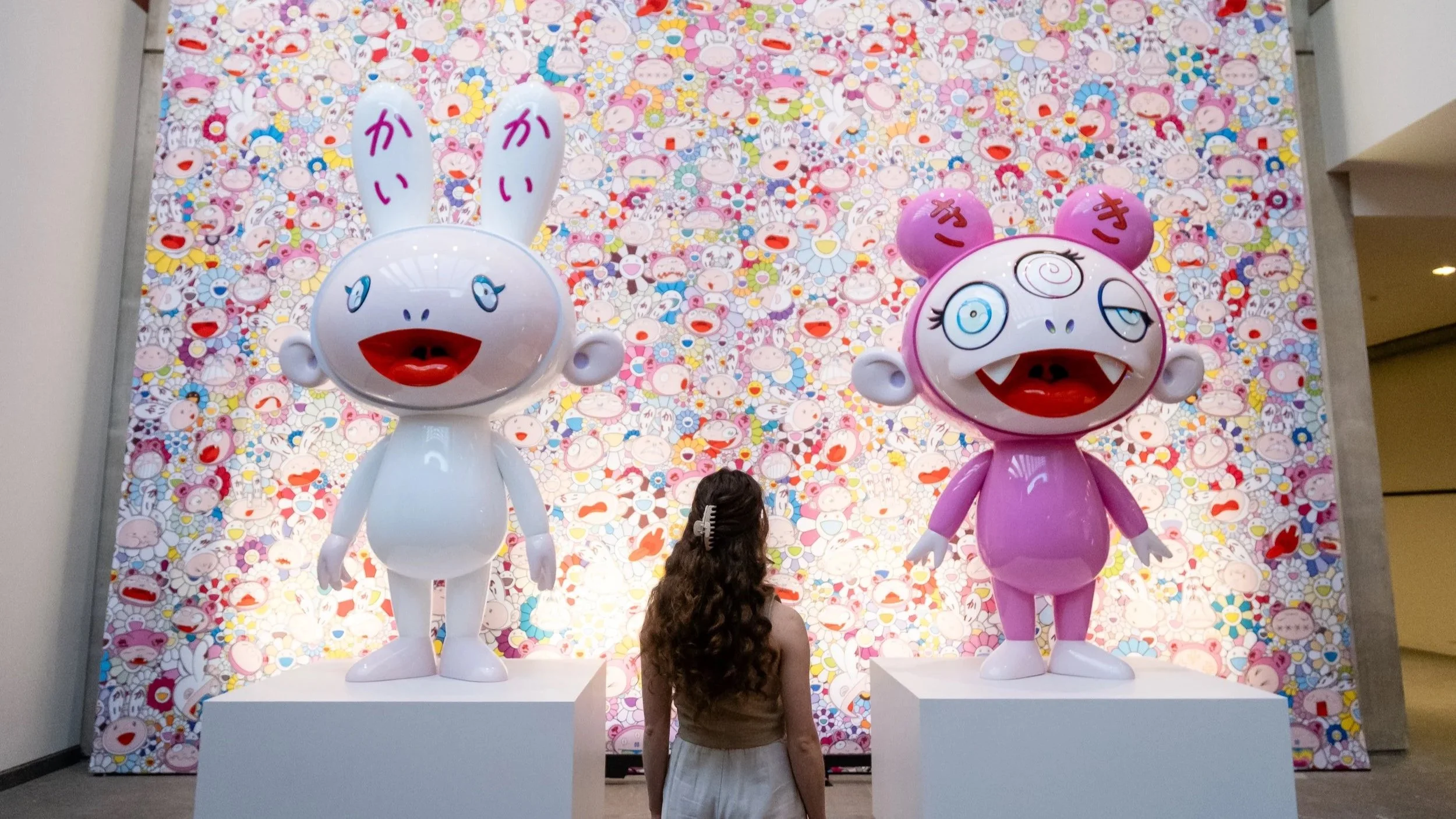 Young woman standing in front of sculptures and art created by Takashi Murakami for an opening exhibit