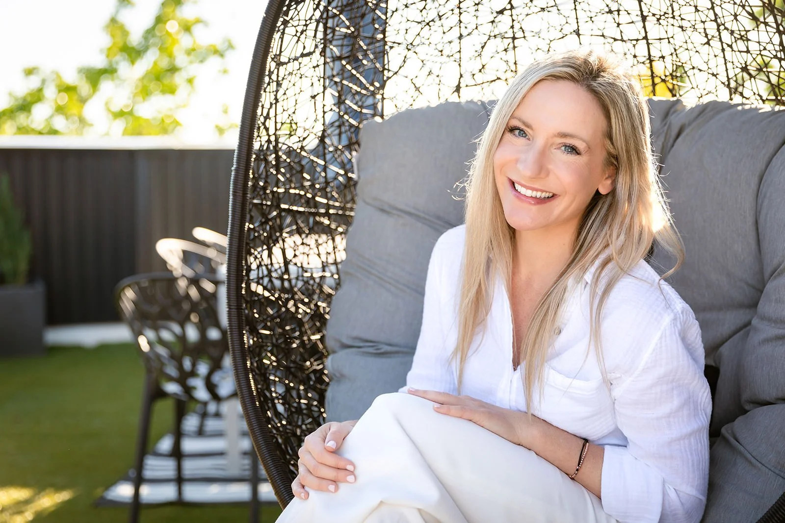 Christina Campbell sitting in a stylish outdoor space on a hanging chair, radiating warmth and authenticity as part of her personal branding for real estate.
