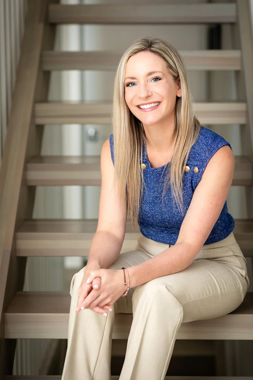 Christina Campbell, dressed in professional attire, seated on modern wooden stairs, showcasing her polished and approachable style as a real estate agent.