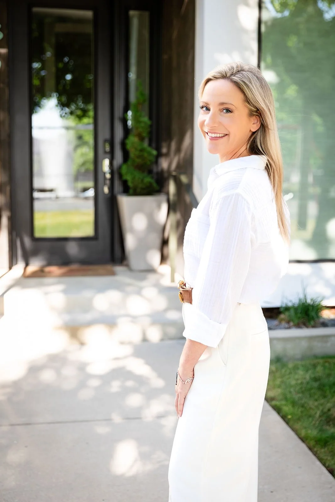 Christina Campbell smiling and looking back while standing near the front door of a beautifully landscaped home, reflecting her dedication to guiding clients in their home-buying journey.