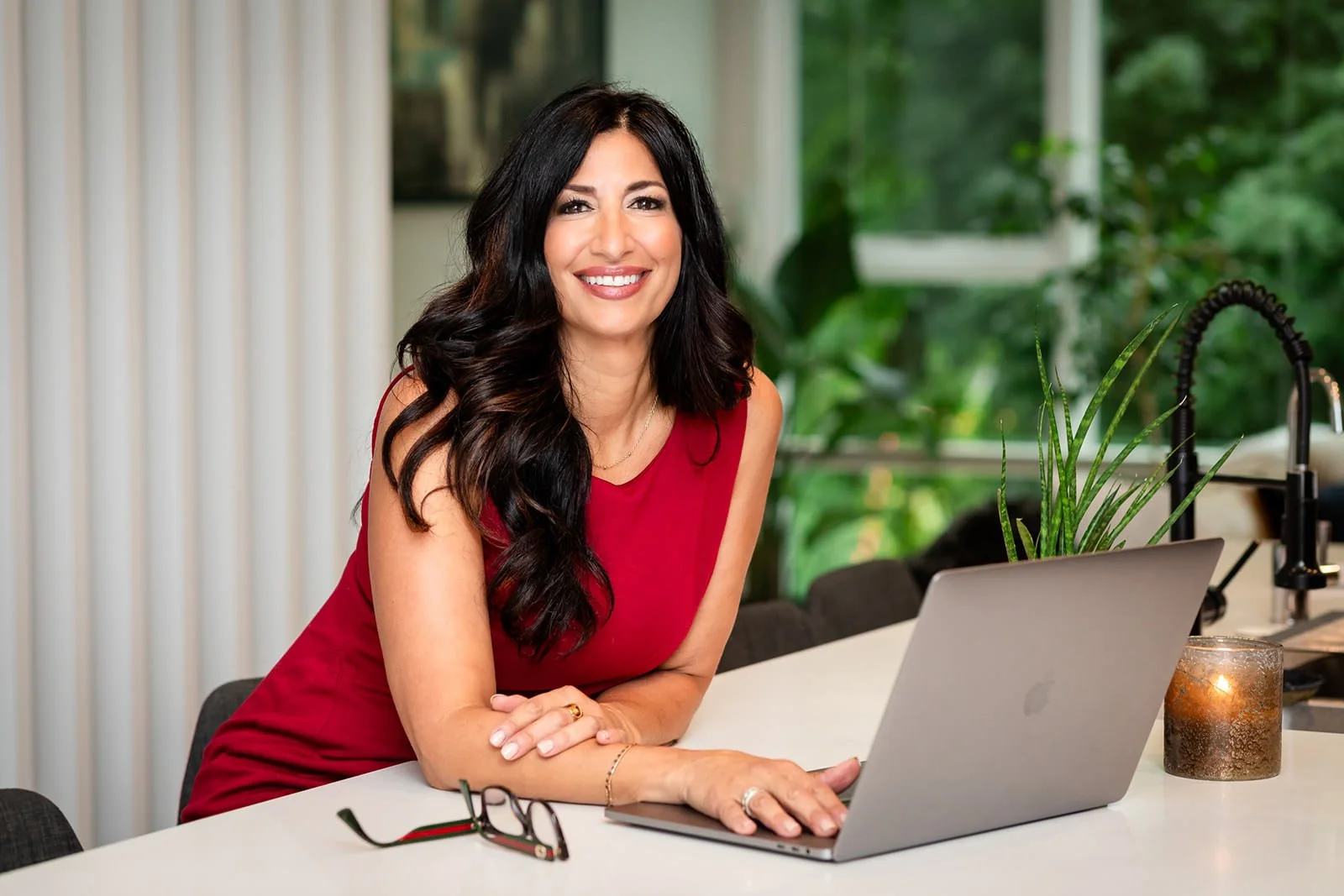 Frances DiBello, business consultant, smiling at the camera while working at her laptop in a bright kitchen, illustrating her strategic yet approachable work style.