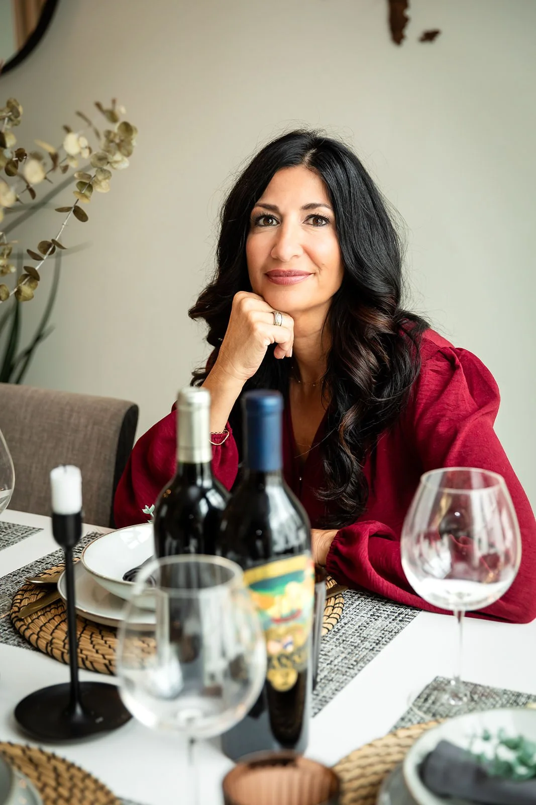 Frances DiBello, IT and business strategist, seated at a tastefully set table with wine bottles, embodying a blend of elegance, warmth, and professionalism.