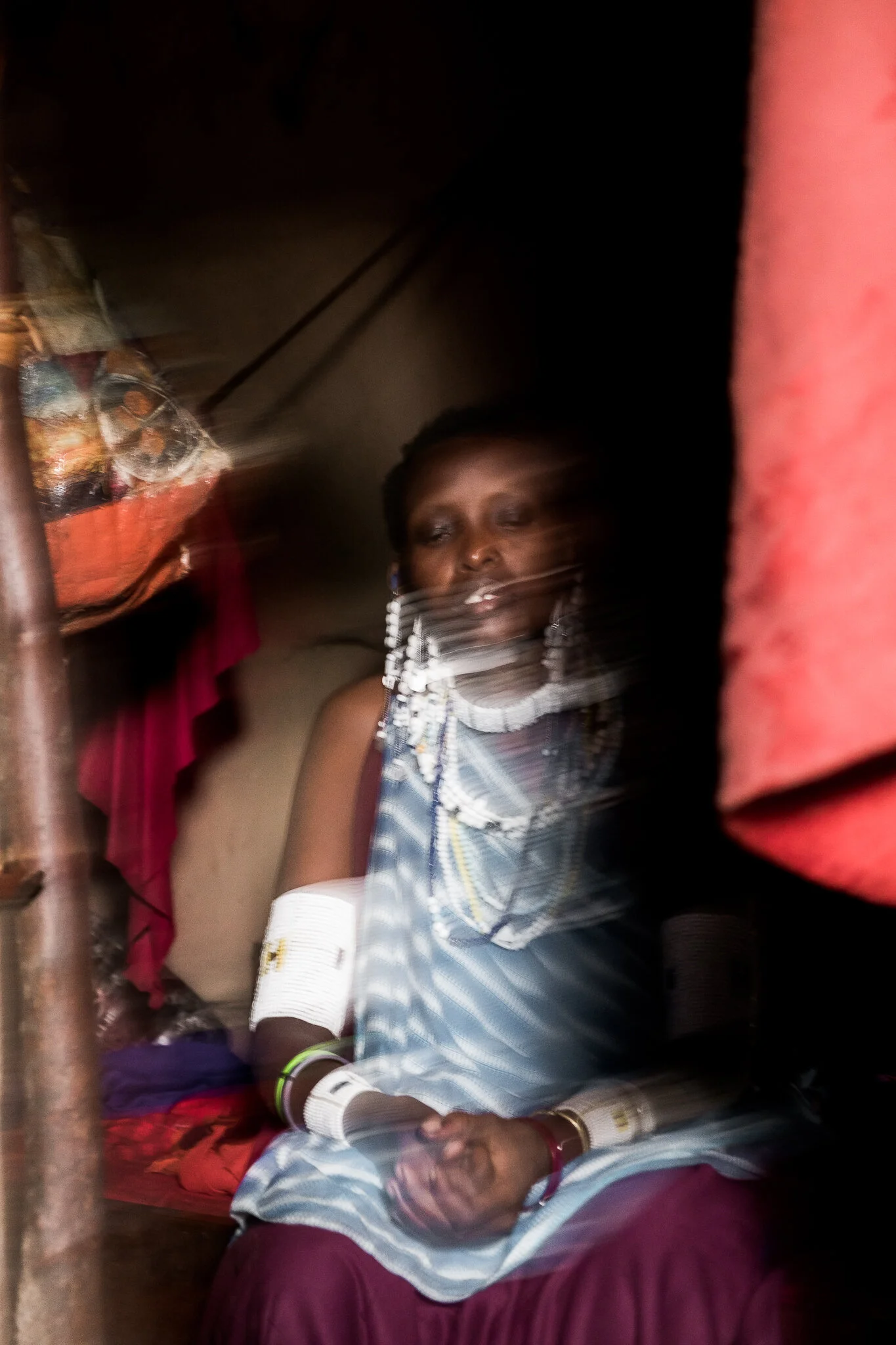 A blurry image of a Maasai woman in Tanzania in her tent shows her jewelry and beautiful blue and purple clothing