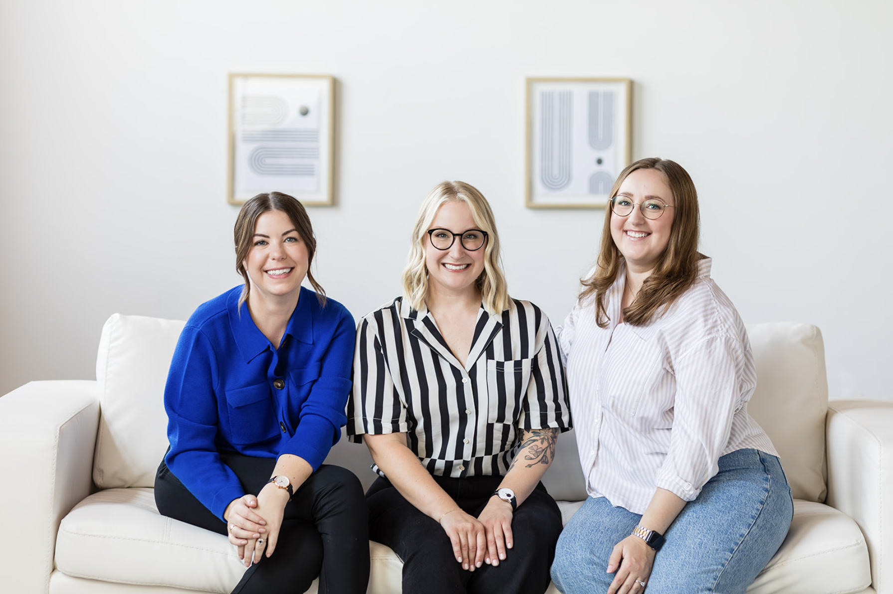 The Walder Studio team poses together on a white couch in a bright, modern space. The three women, dressed in stylish yet professional attire, smile confidently, reflecting their collaborative and creative approach to branding and design.