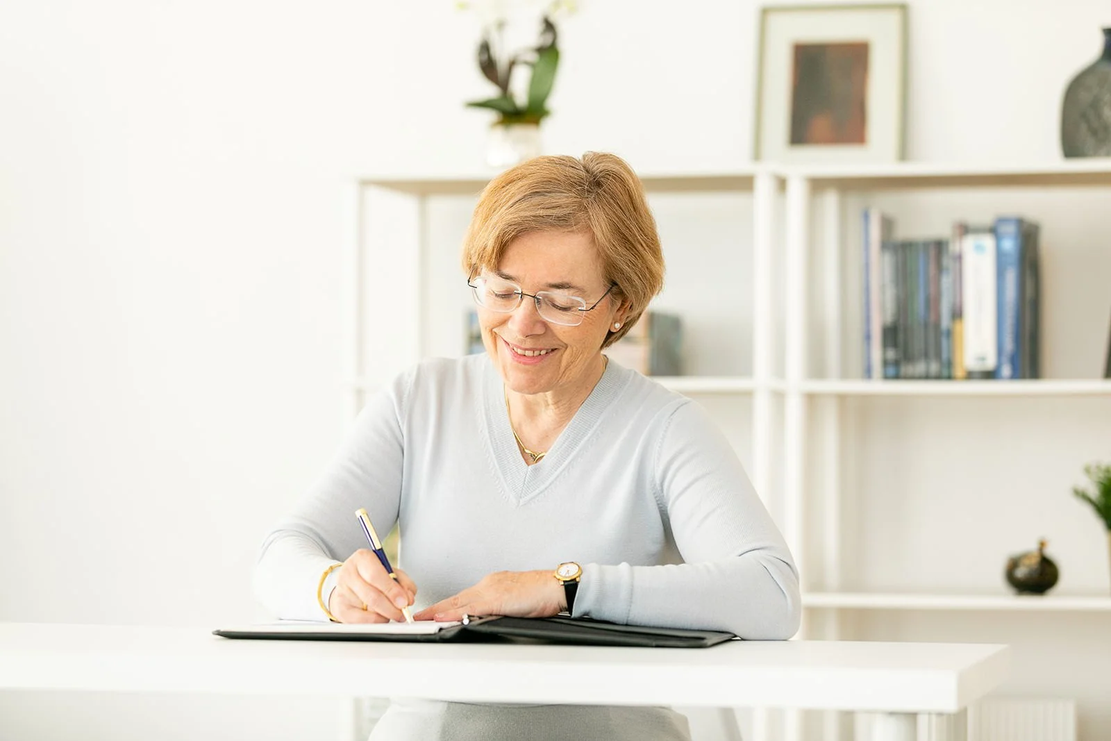 Dr. Brigitte Apfel writing in a notebook at a bright, modern desk—capturing a candid moment of reflection during her personal brand photography session for licensed mental health professionals.