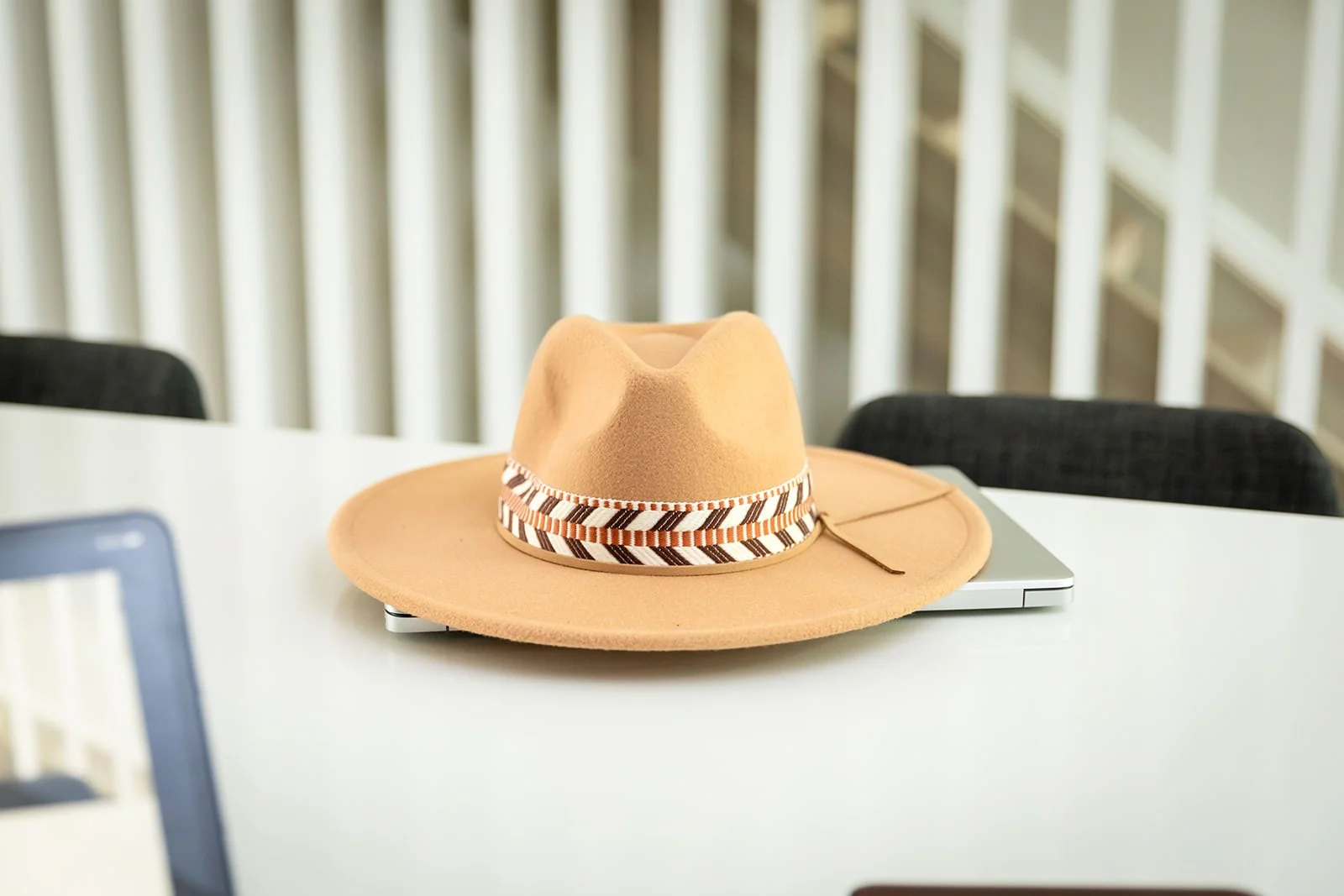 A stylish wide-brimmed hat resting on a laptop on a modern white desk, symbolizing travel readiness and exploration.