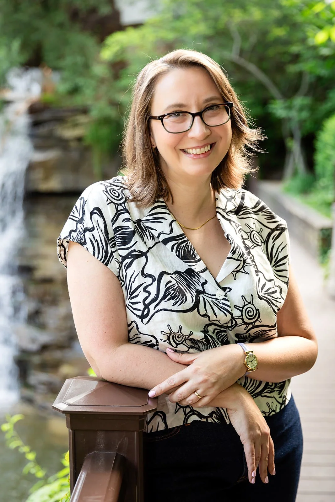 Jessica Gaya, Cleveland travel advisor, smiling confidently while leaning on a wooden railing with a lush green waterfall background.