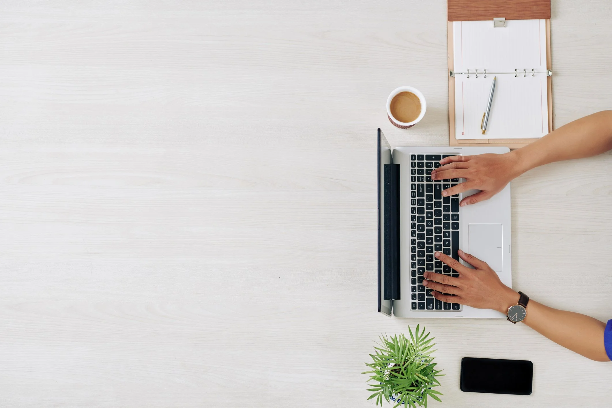 overhead image of hands typing on a macbook next to a cup of coffee and a planner