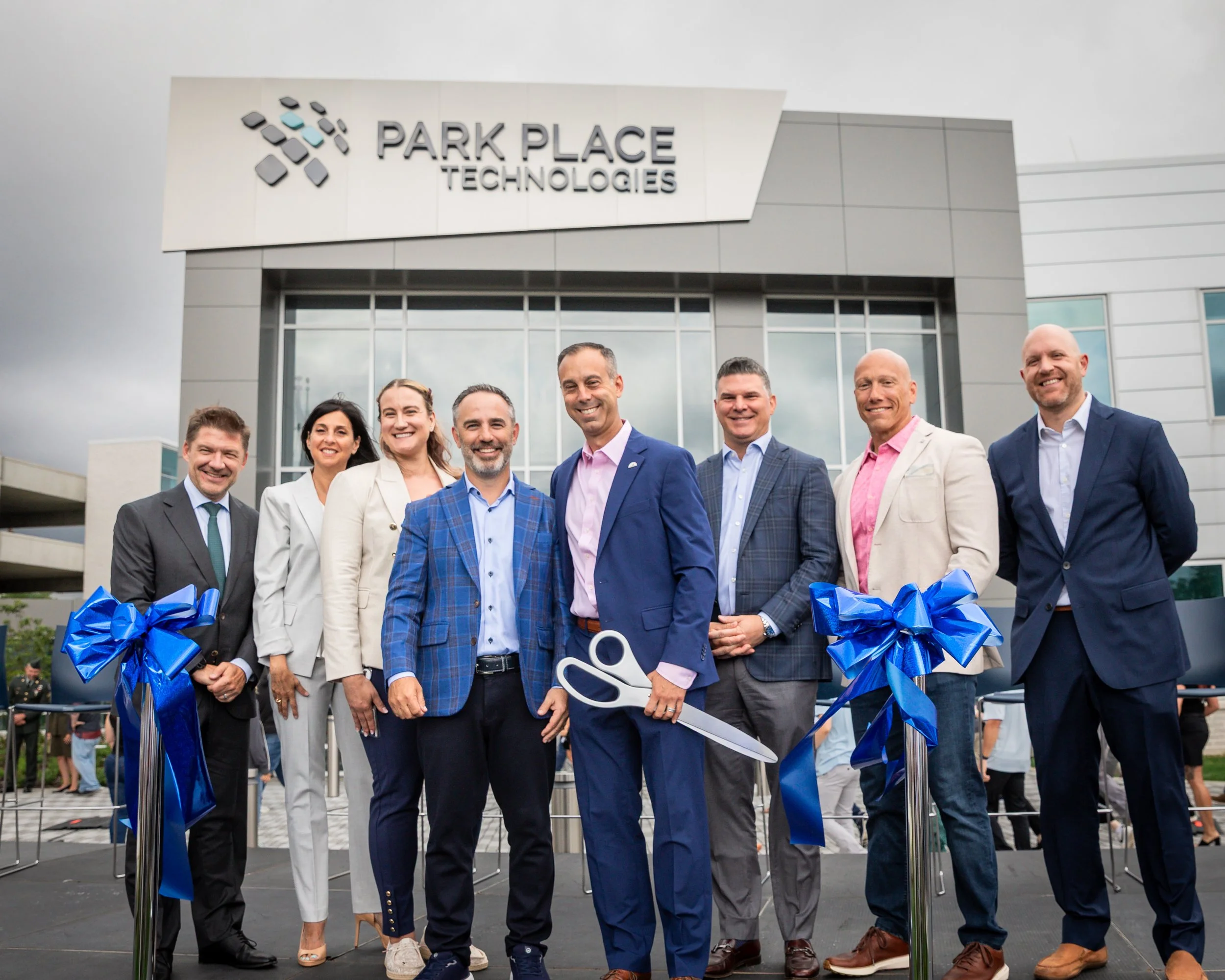 A group of men and women wearing professional business attire smile after a ribbon-cutting ceremony for a new office inauguration and open house in Ohio