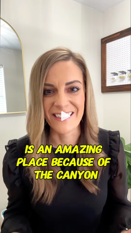 A woman with long blonde hair smiling at the camera, wearing a black top with ruffled sleeves, in a room with a mirror and a wooden-framed bulletin board in the background, with yellow text overlay saying 'IS AN AMAZING PLACE BECAUSE OF THE CANYON'.