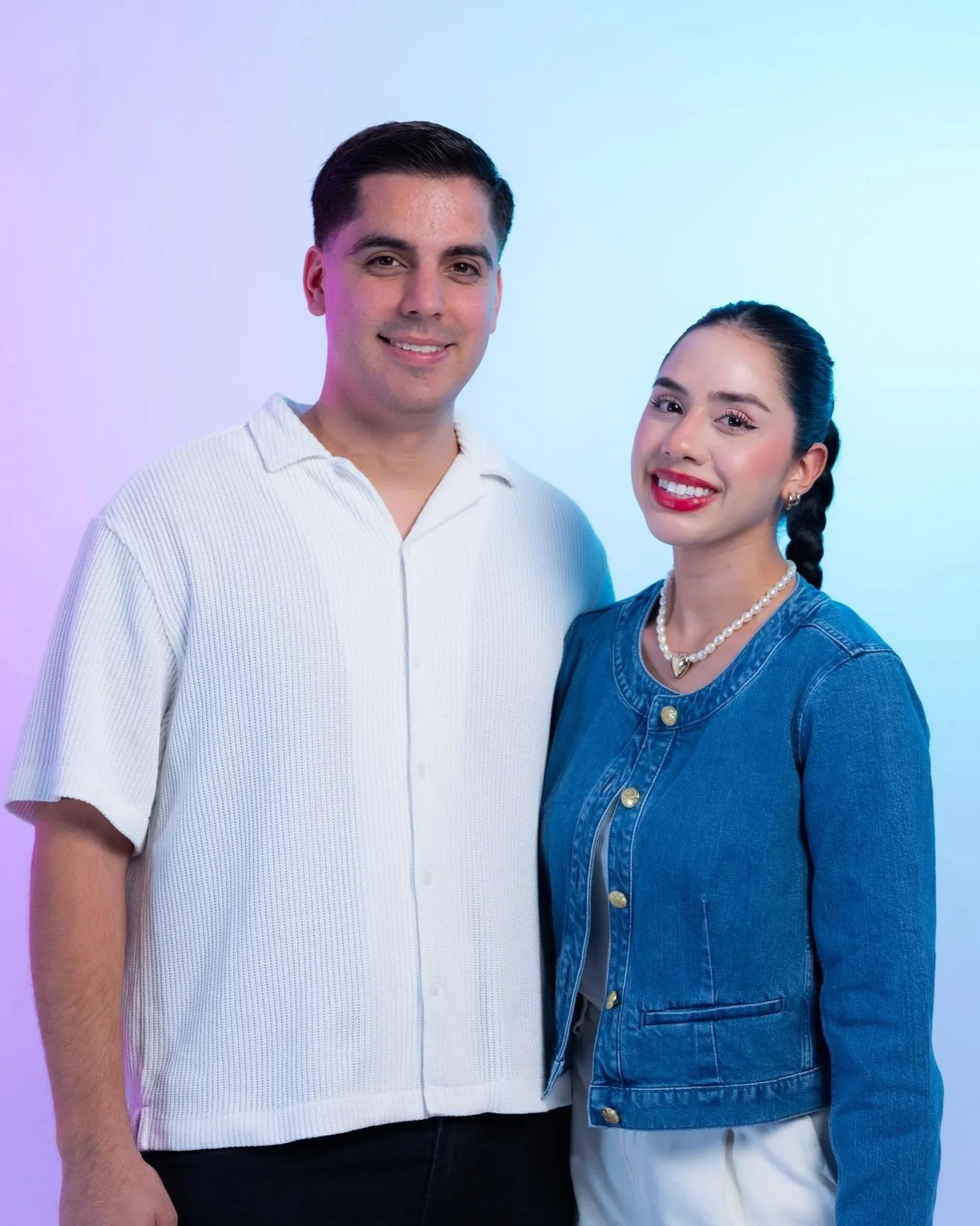 A man and a woman smiling, standing close together against a colorful background.