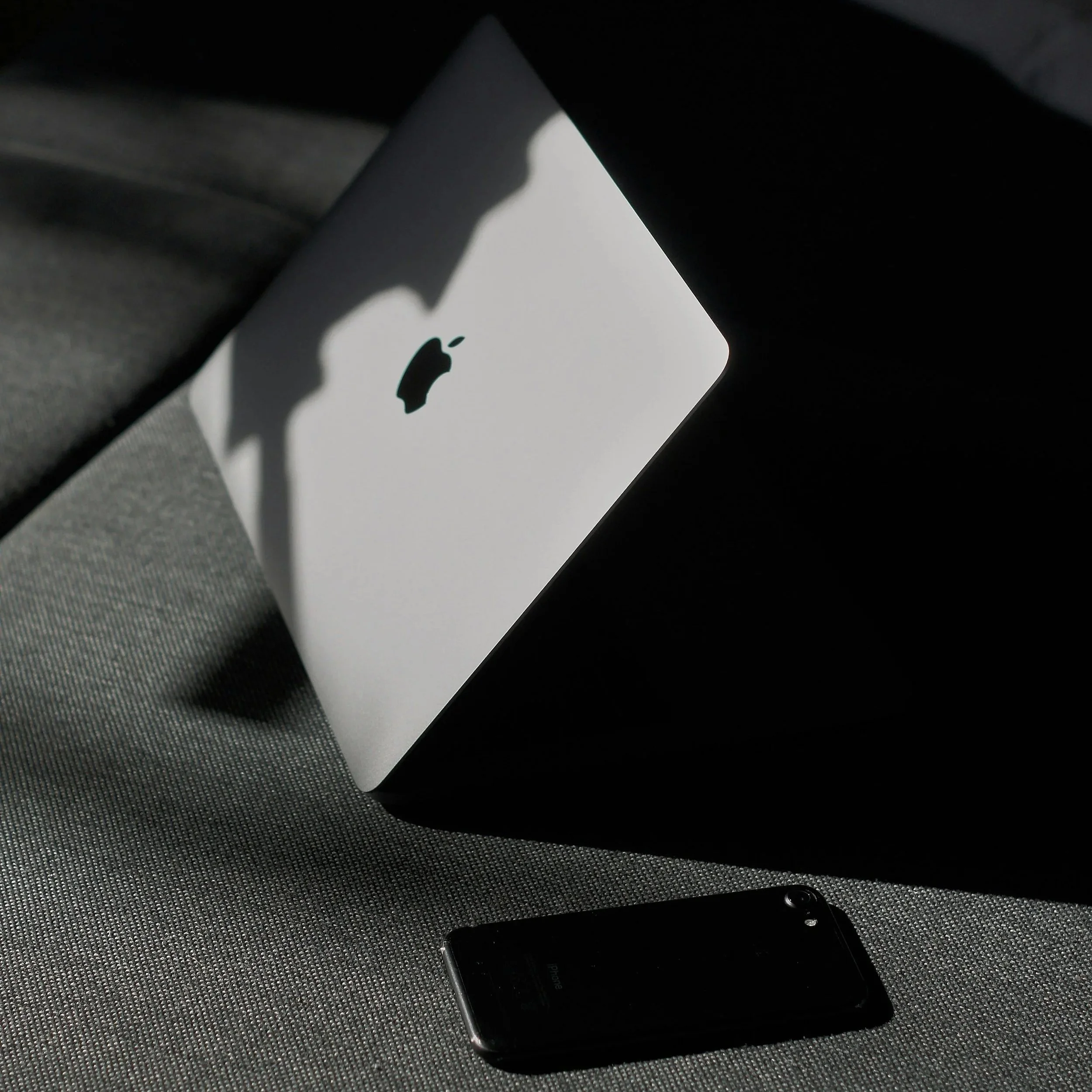 An iPhone lying on a dark textured surface with a white box reflecting the Apple logo behind it.