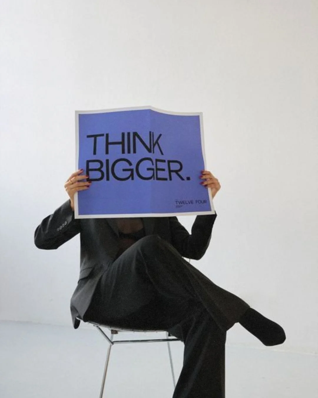 a marketing professional sitting in a chair holding a newspaper that reads Think Bigger at a brand identity photoshoot