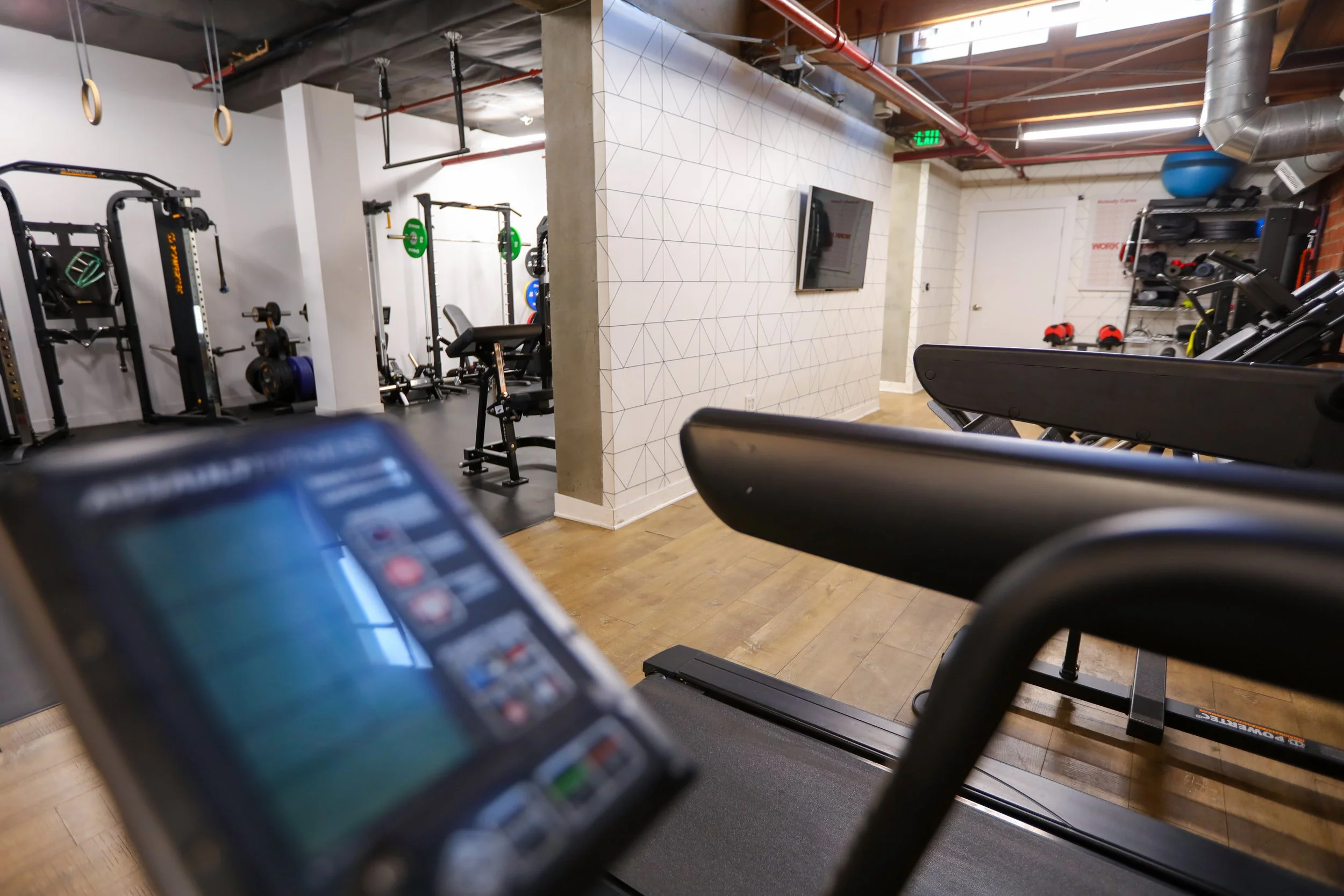Interior of a modern gym with treadmills, weightlifting equipment, and a TV on the wall.