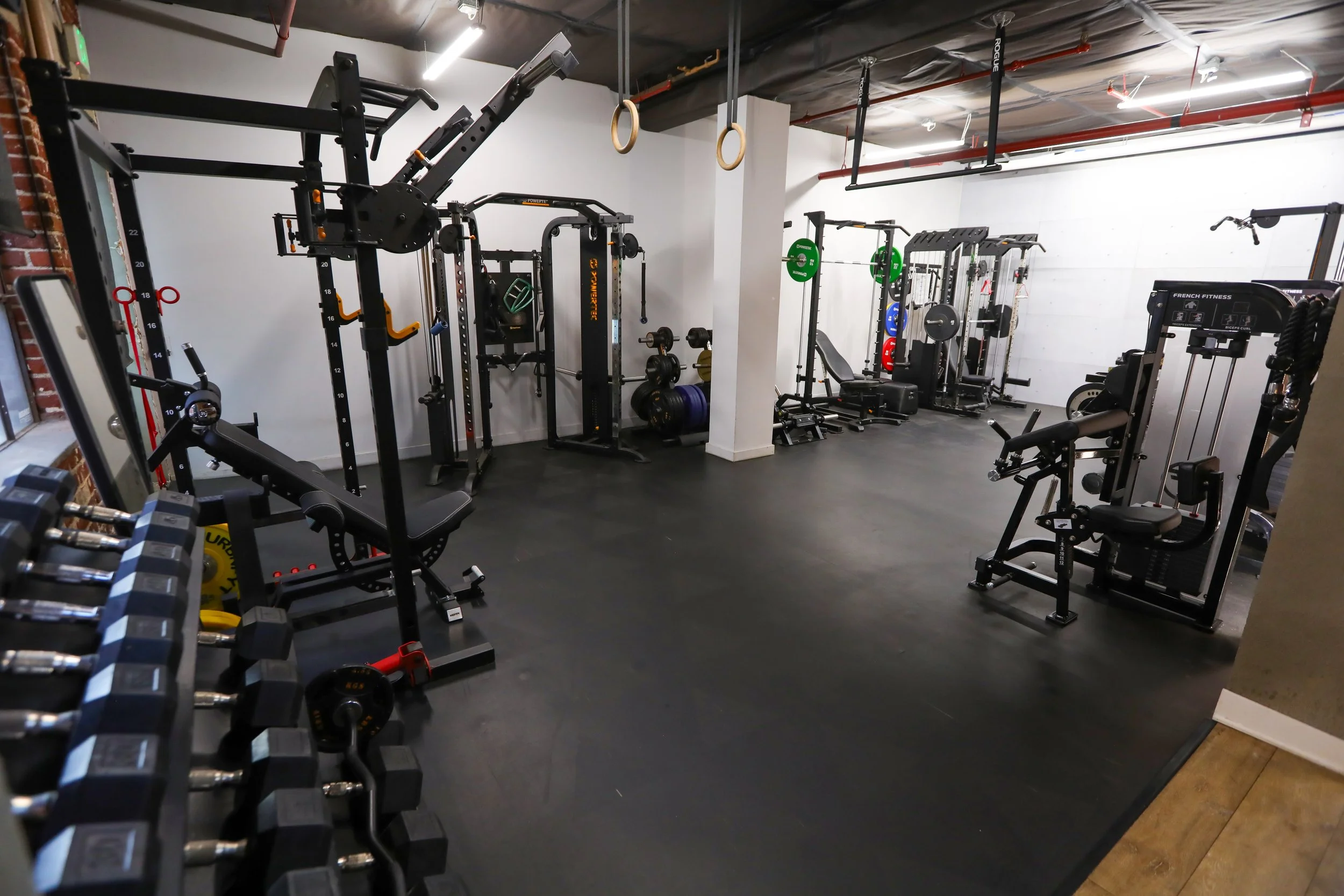 Fitness gym with workout equipment including dumbbells, weight machines, and gymnastic rings in a modern industrial-style space.
