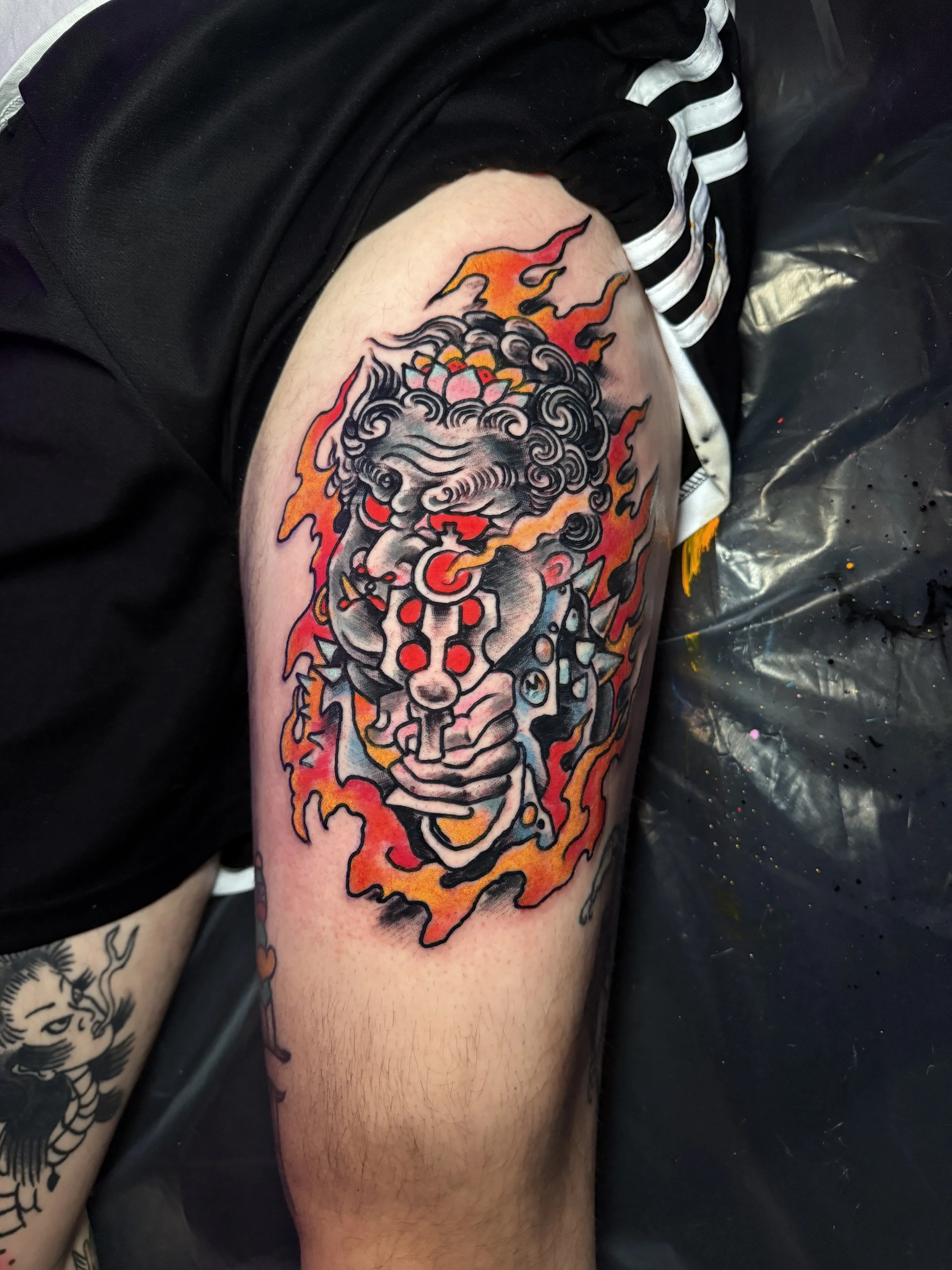 Tattoo of a mythological or traditional figure holding a trumpet, with swirling hair, surrounded by flames, on a person's upper arm.