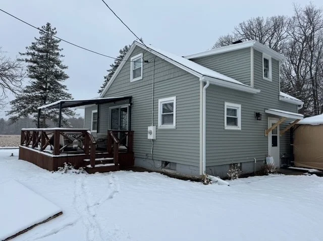 A gray two-story house with a small front porch and snow-covered yard in winter.