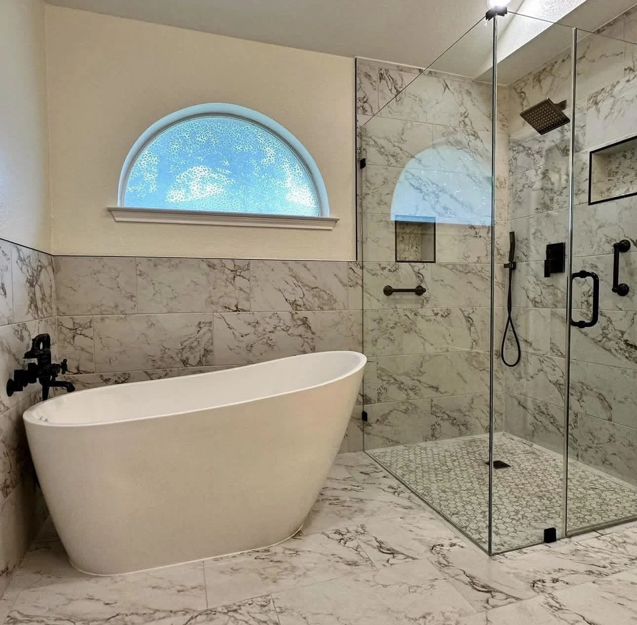 Modern bathroom featuring a white freestanding bathtub and a glass-enclosed walk-in shower with marble tiles.