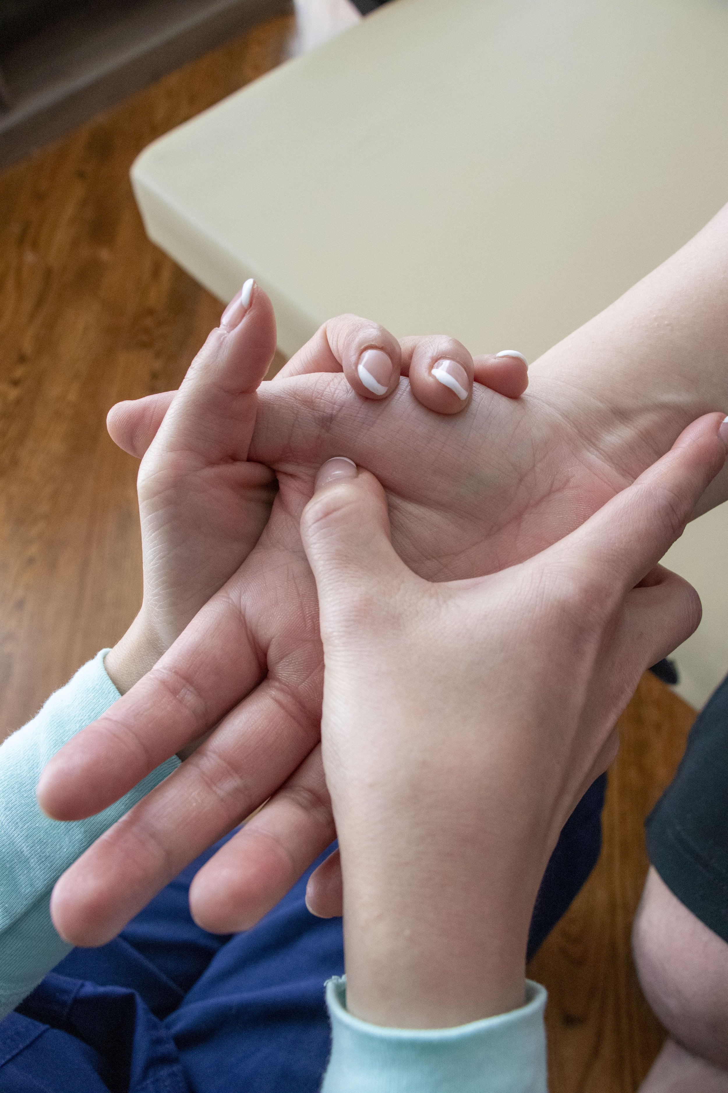 Patient receiving osteopathy on their hand, with a wooden floor and a beige table in the background.
