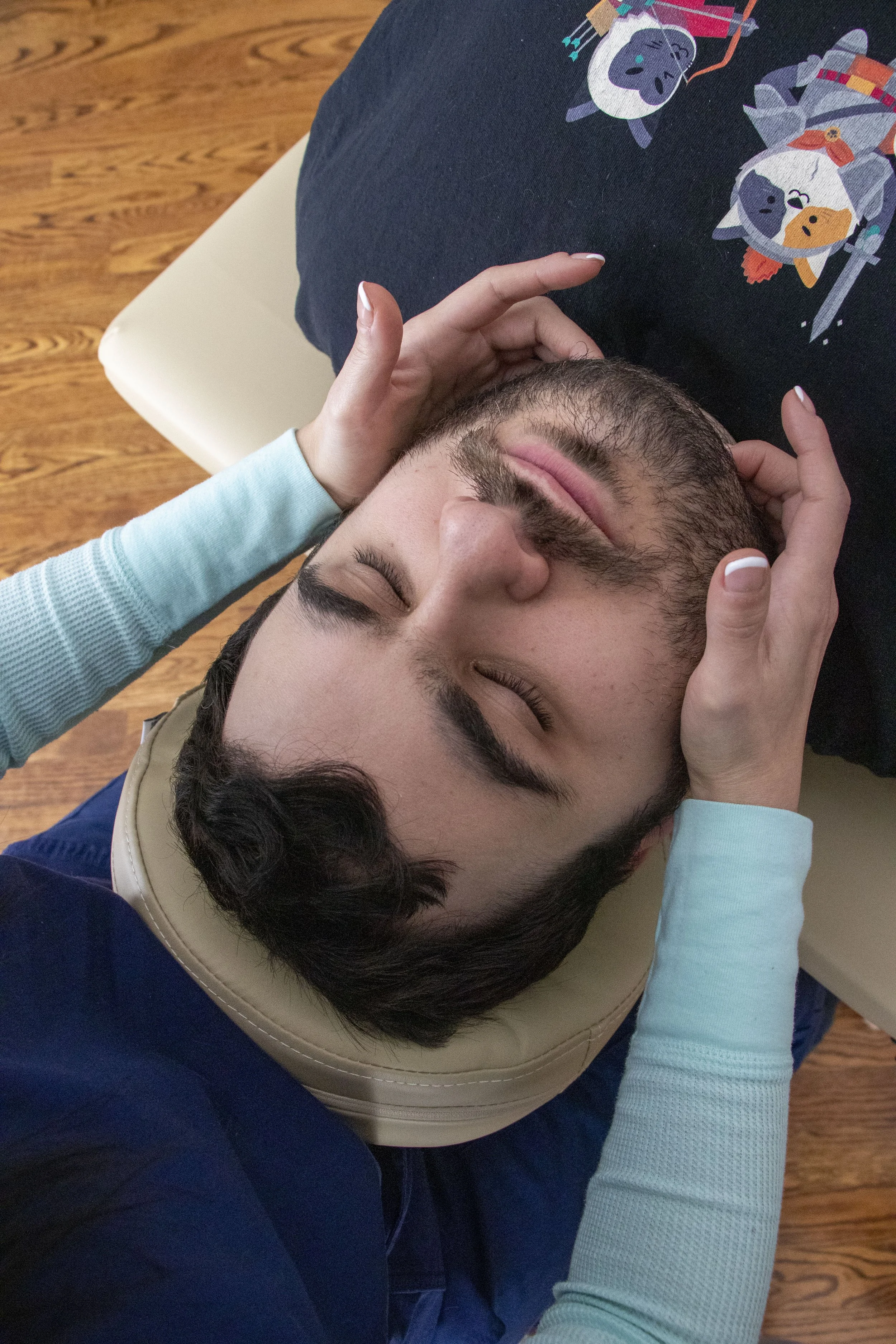 A person lying on a massage table with a cushion supporting their head, receiving a head or face massage from a doctor.