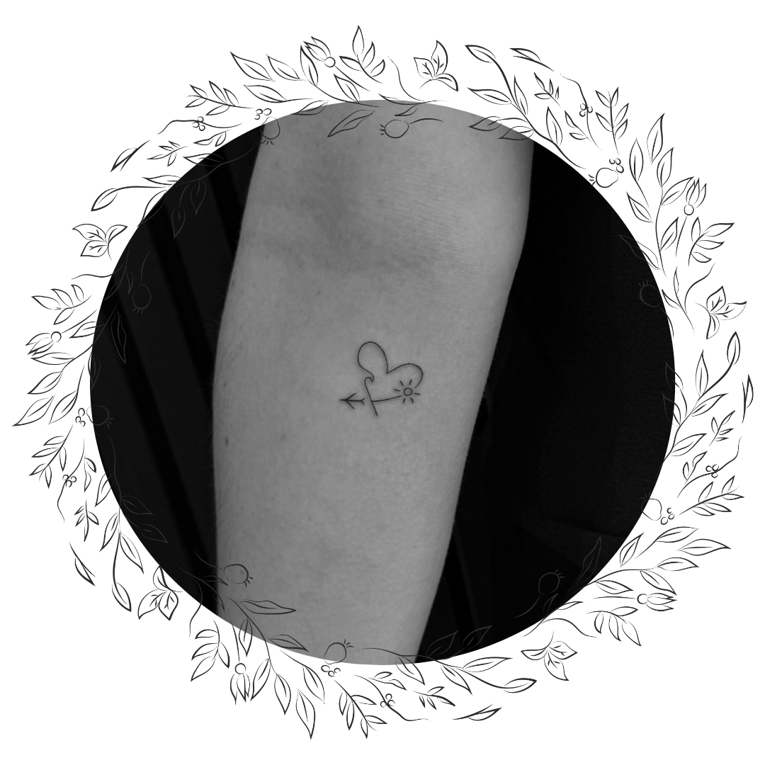 A tattoo of a heart with an arrow through it, a sun, and a small flower on a person's forearm.