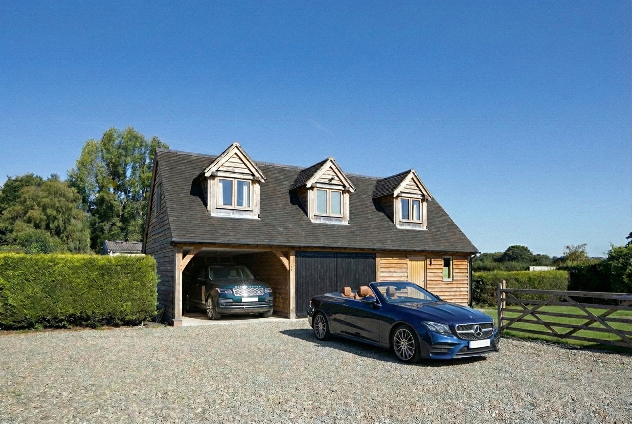 Triple bay oak garage with a room over, featuring dormer windows and classic timber cladding.