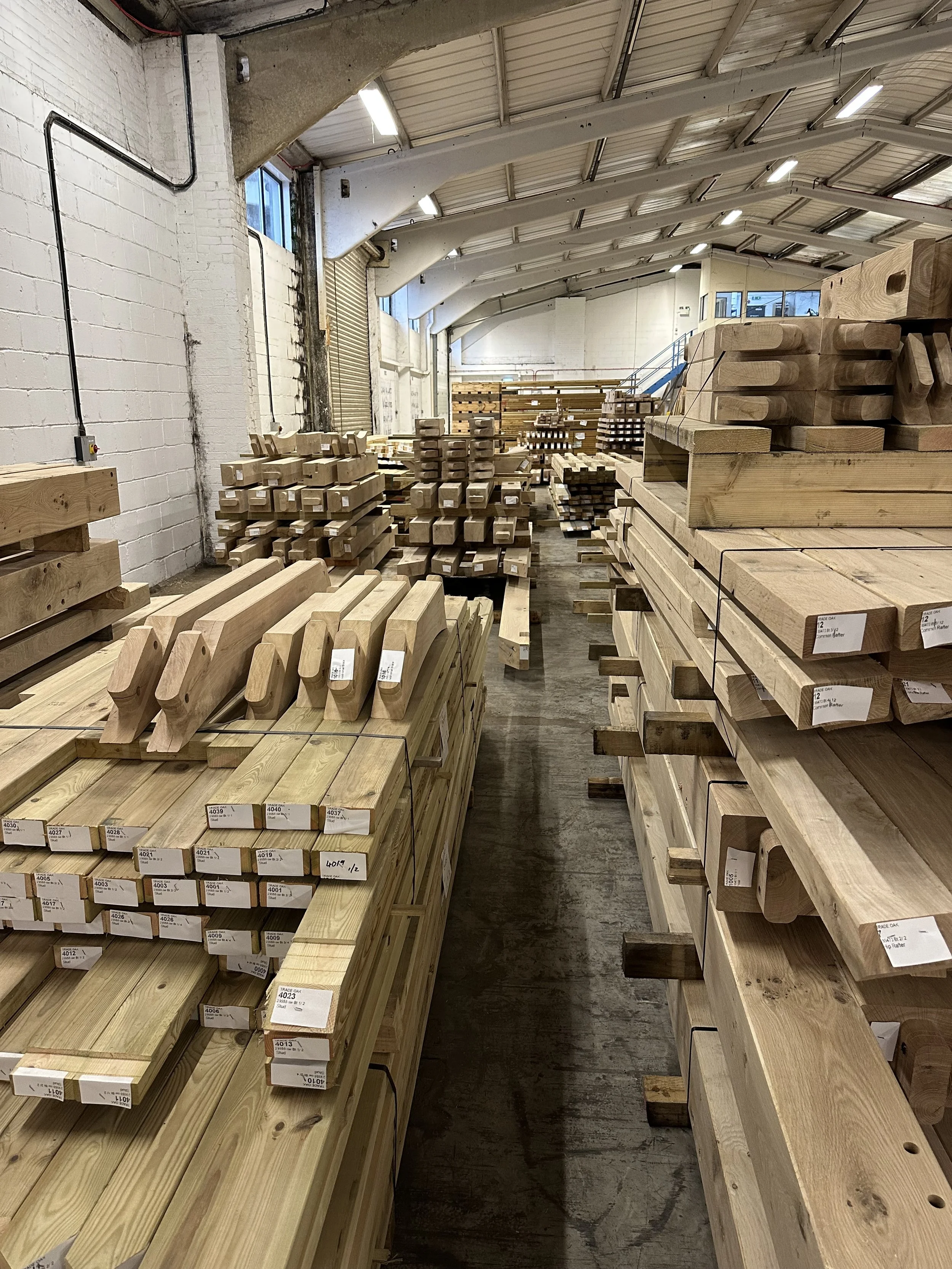 A hardware store with lots of wooden lumber stacked on shelves and pallets inside a warehouse.