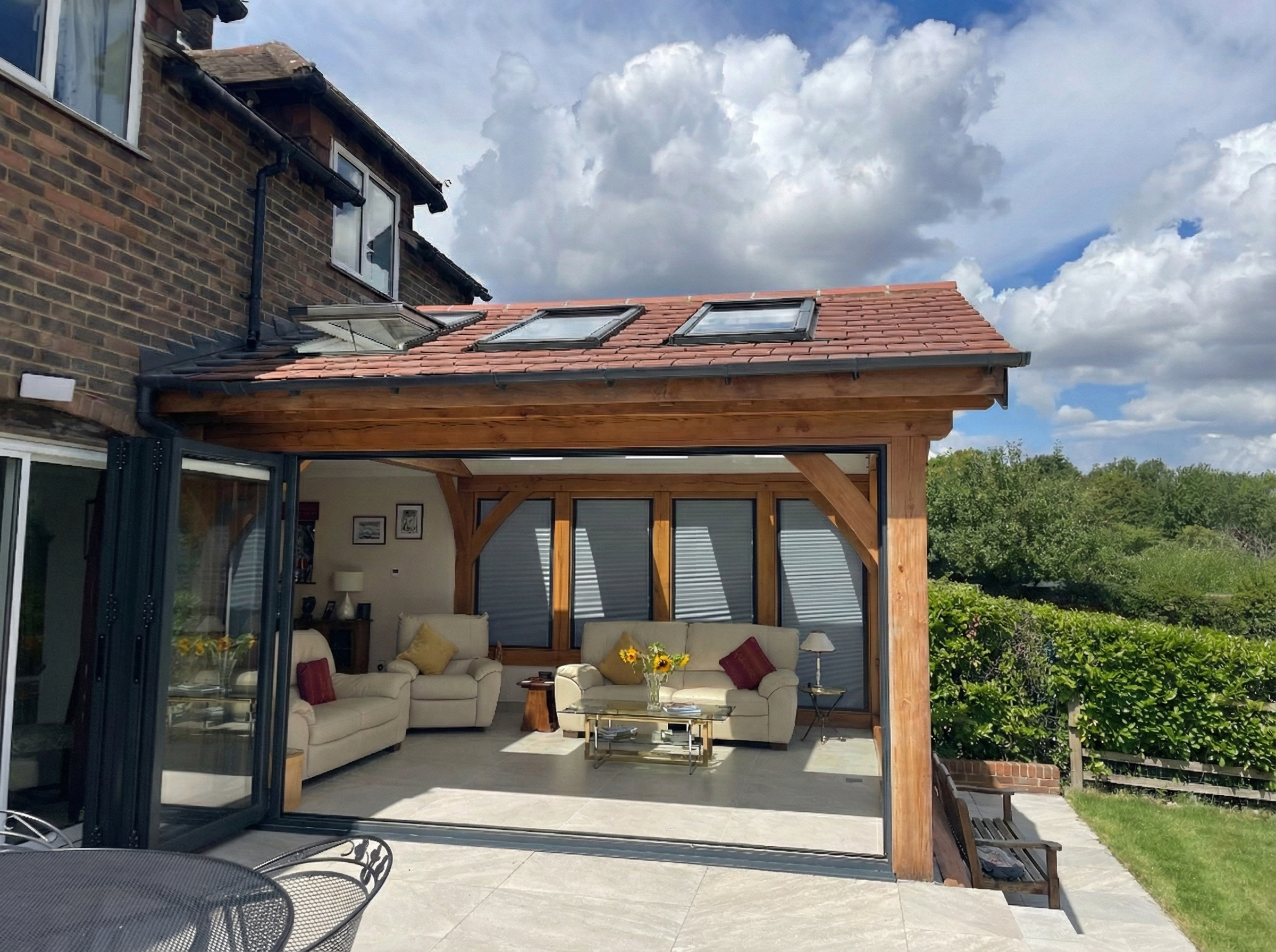A bespoke oak sunroom extension with open glass doors leading to an outdoor patio area