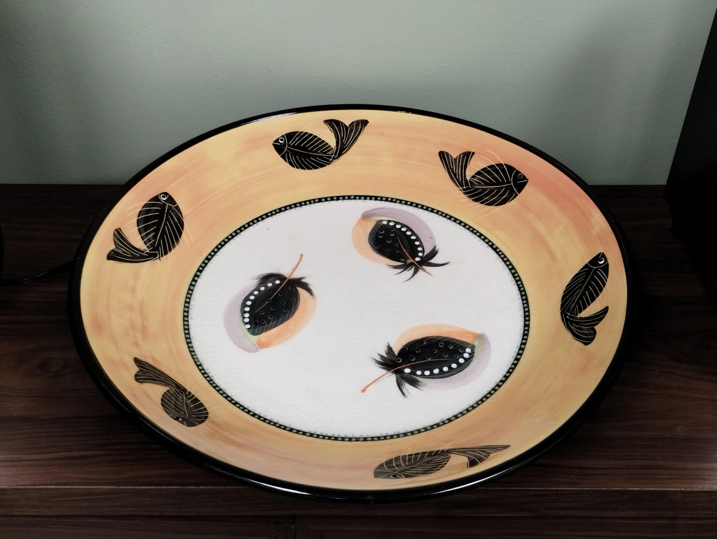 A large artisan bowl, part of the calming decor at Resting Squirrel. The center is decorated with three feathers and the yellow rim with six fish alternating to face towards and away from a neighbor.  Perhaps this used to be a bird bath.