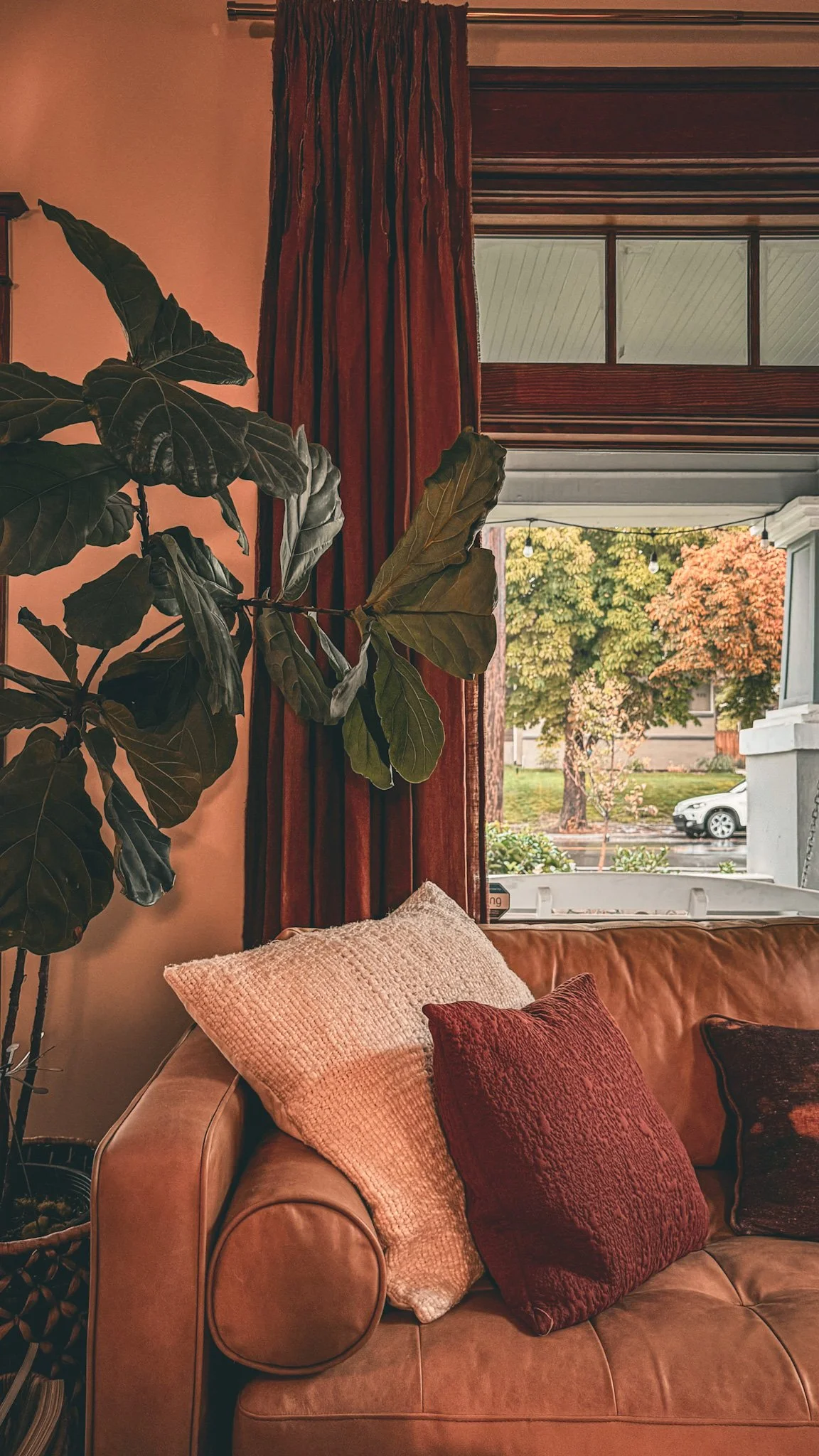 Warm sitting area at 930 South with a rust-colored chair, layered pillows, houseplant, and daylight from a nearby window.