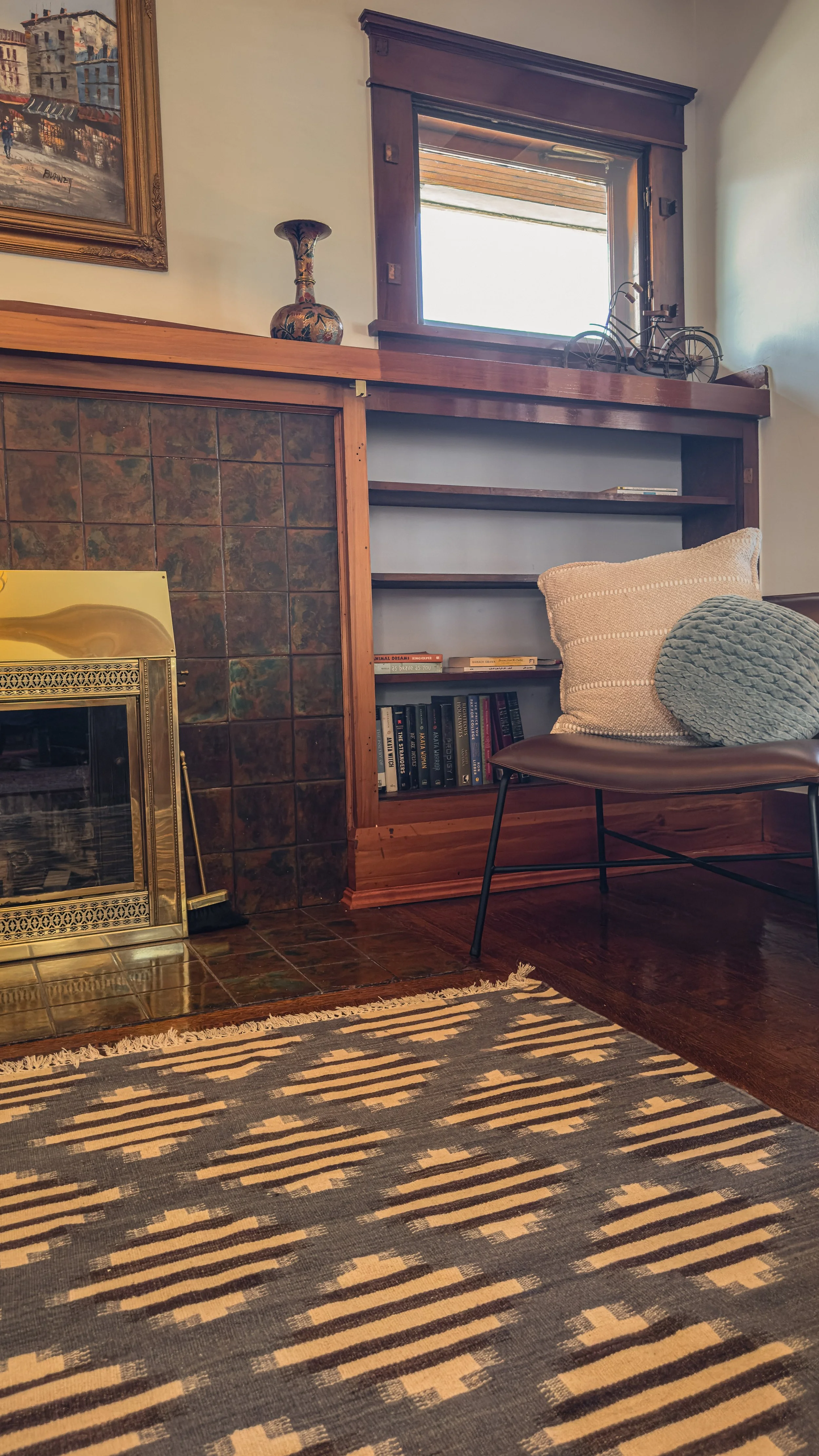 Living room corner with tiled fireplace, built-in shelving, wood trim, and lounge chair in the Emerson residence.