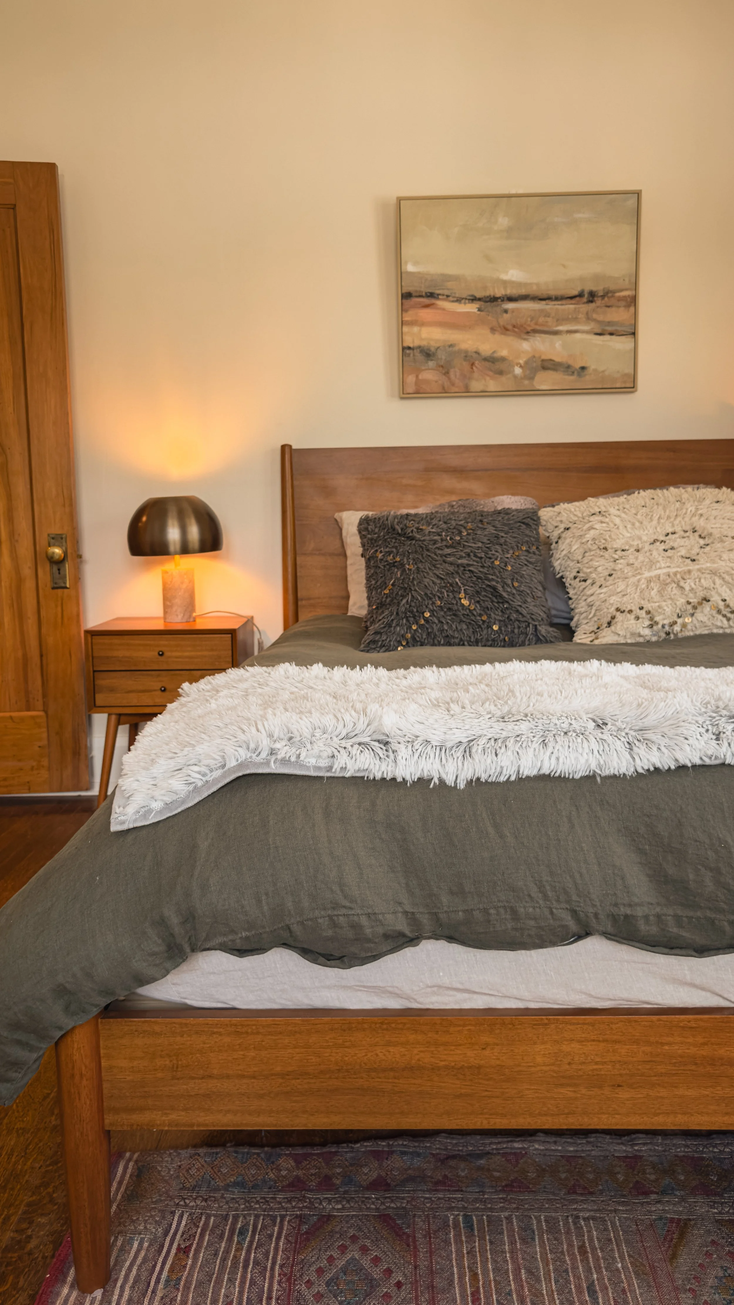 Bedroom with wood bed frame, layered neutral bedding, bedside table, and warm lamp light in Salt Lake City.