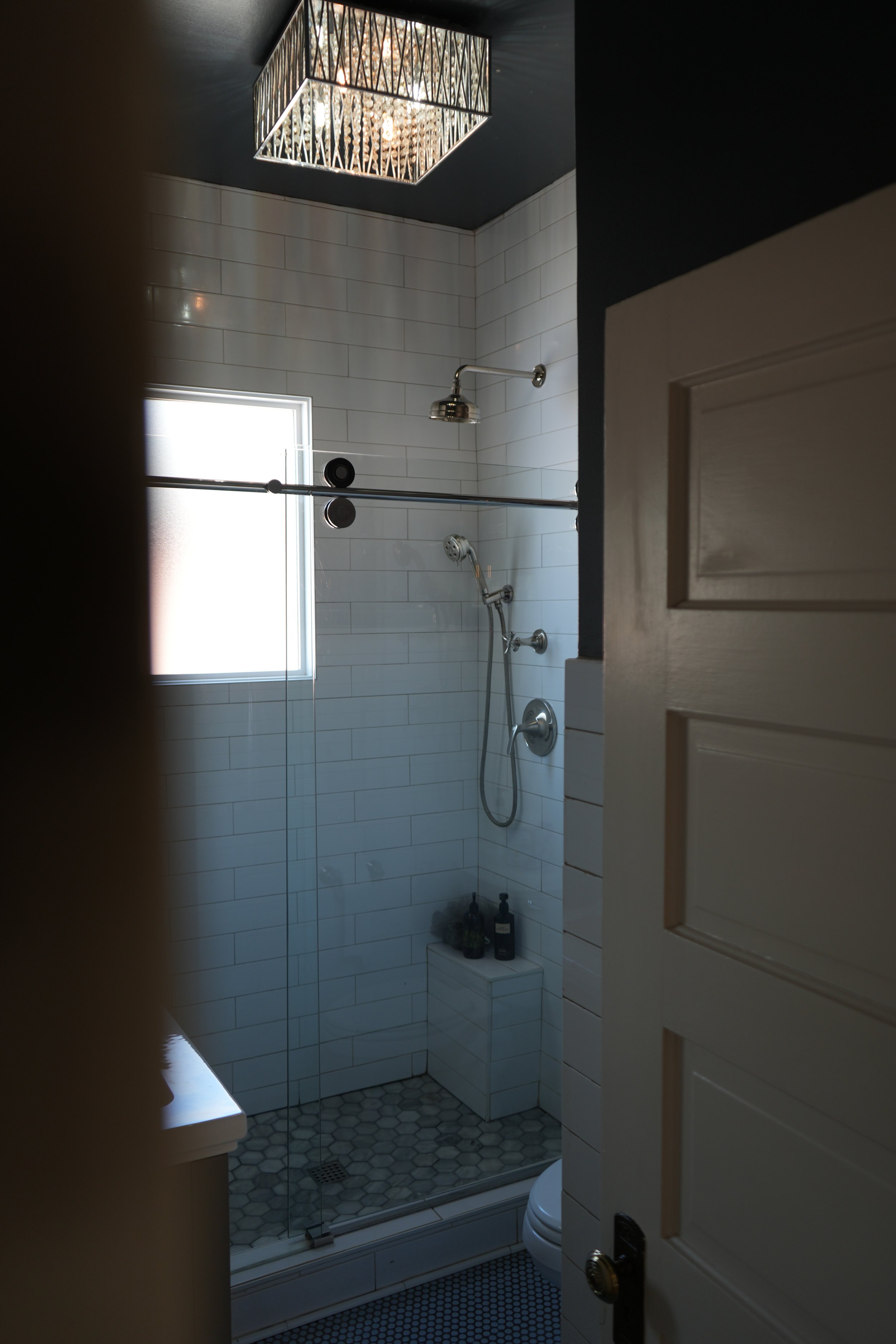 Bathroom at 930 South in Salt Lake City viewed through a doorway, with a tiled walk-in shower, glass enclosure, rainfall showerhead, and patterned tile floor.